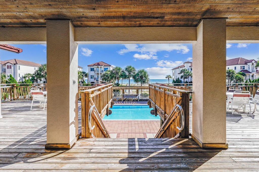 Pool deck with wooden railings, turquoise pool, and ocean view between coastal homes.