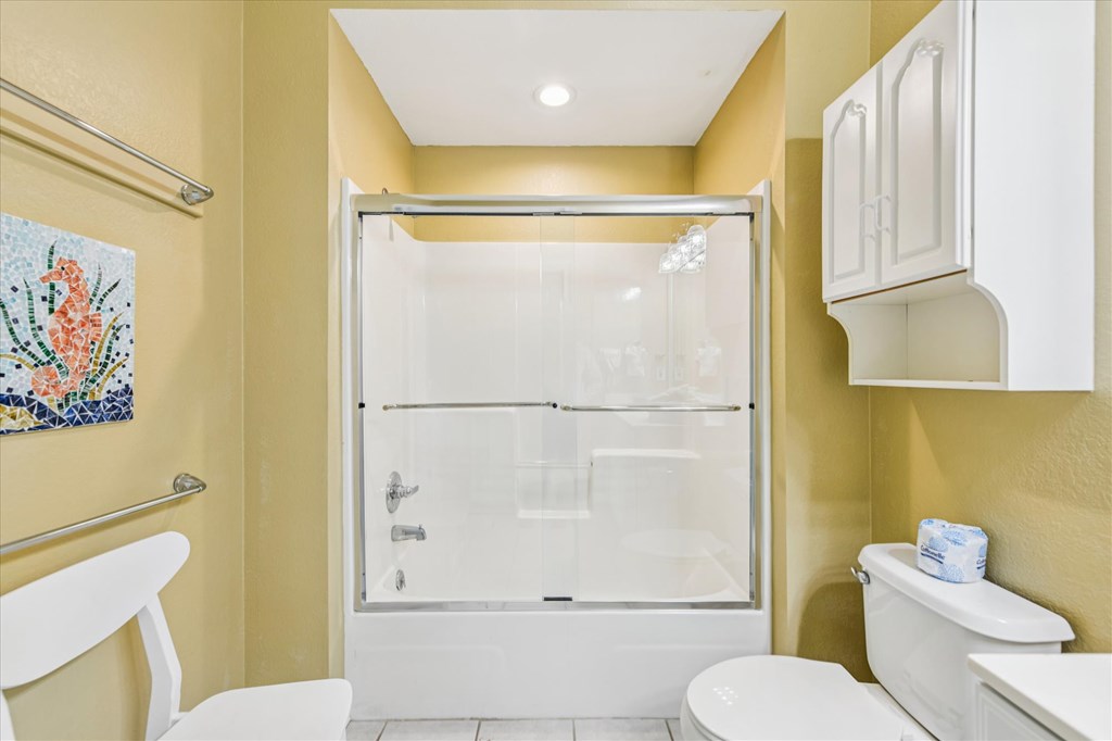 Bathroom with a glass-enclosed tub and shower, yellow walls, and white cabinetry.