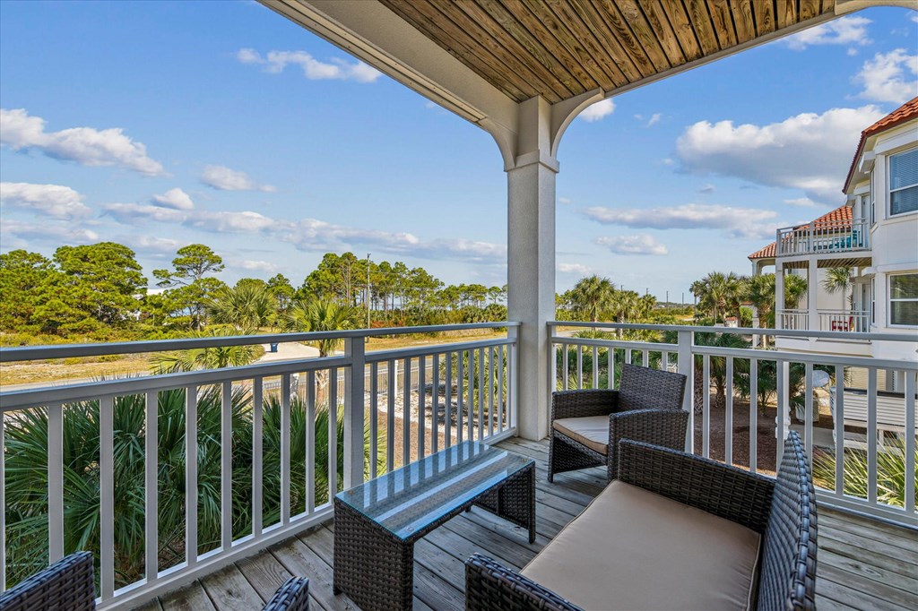 Covered balcony with wicker seating overlooks palm trees and coastal vegetation.
