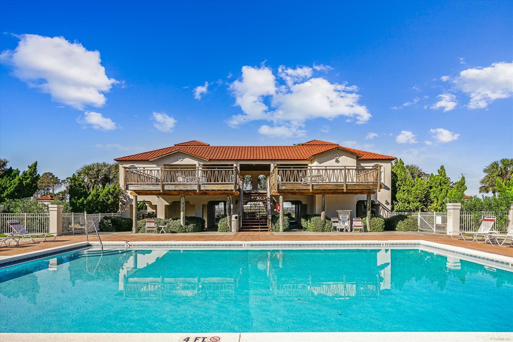 Outdoor pool in front of a raised clubhouse with two wooden-railed balconies.