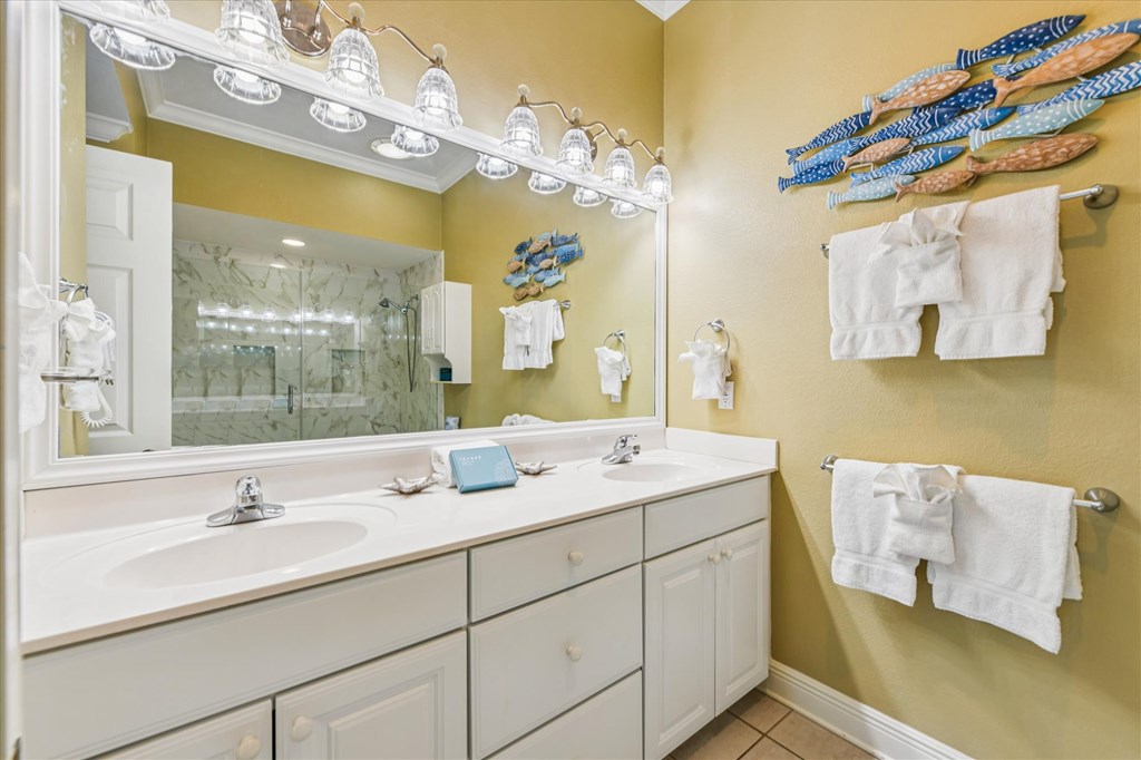 Bathroom with a white double vanity, mirrored lights, and glass-enclosed marble-patterned shower.