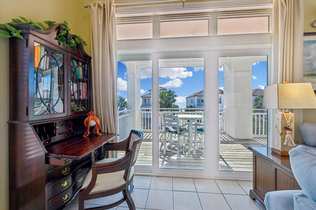Furnished room with a wooden desk and sliding glass doors opening onto a covered balcony.