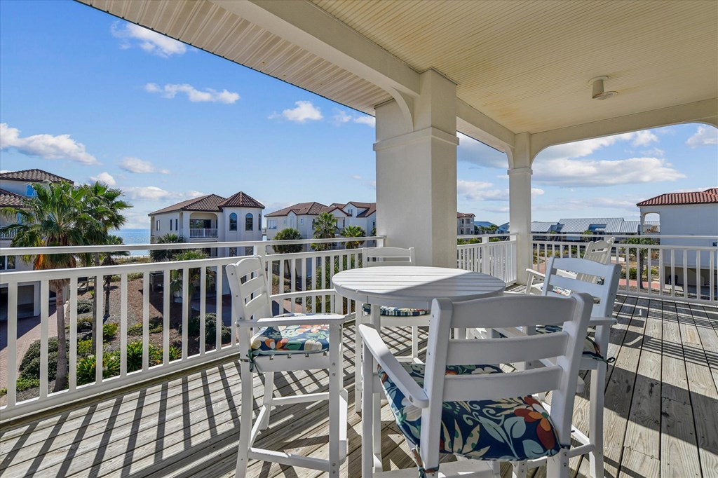 Covered deck with white dining furniture and a glimpse of water beyond neighboring homes.