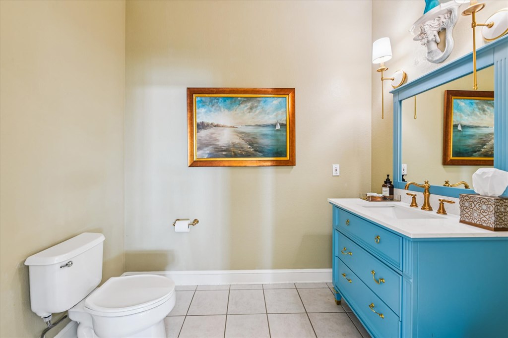 Bathroom with a bright blue vanity, tiled floor, and framed coastal painting.