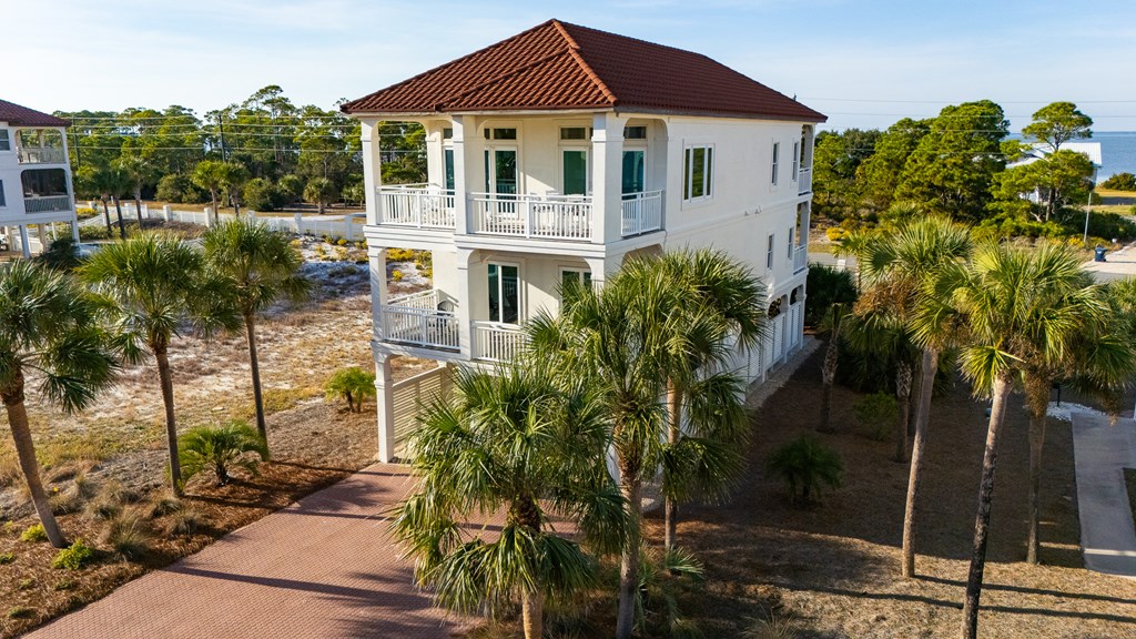 Two-story white coastal house with red tile roof, stacked balconies, and surrounding palm trees.