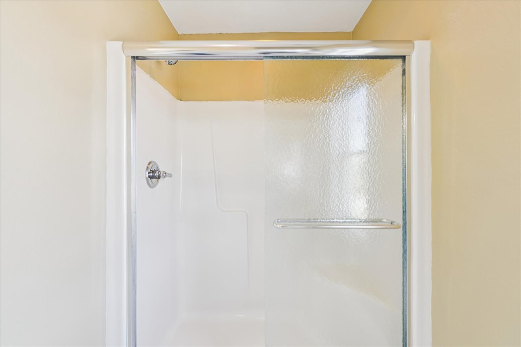 Bathroom shower with a white surround, chrome fixtures, and a sliding frosted-glass door.