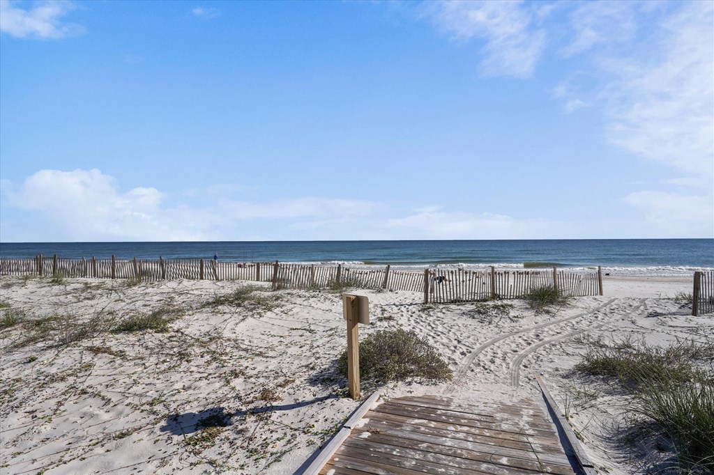 Boardwalk through sandy dunes leading to a fenced beach and ocean.