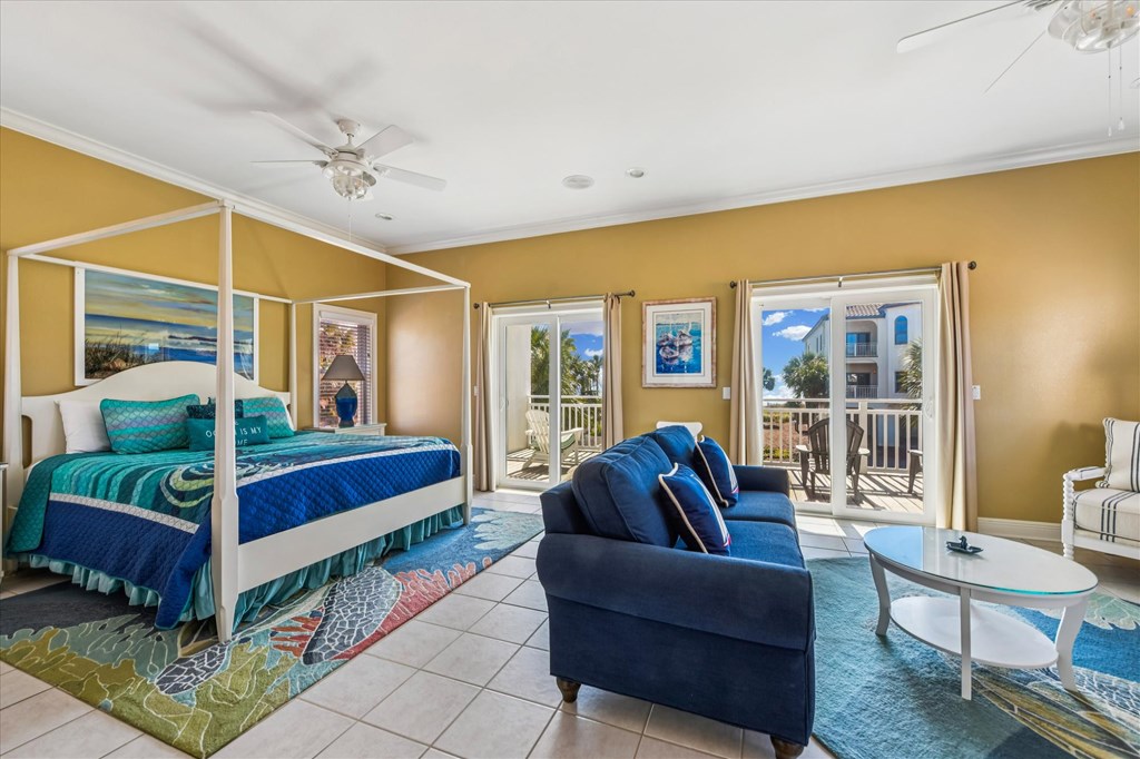 Bedroom with a white canopy bed, blue bedding, and a sitting area beside balcony doors.