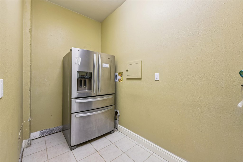 Stainless steel refrigerator in a small kitchen alcove with pale yellow walls and tiled floor.