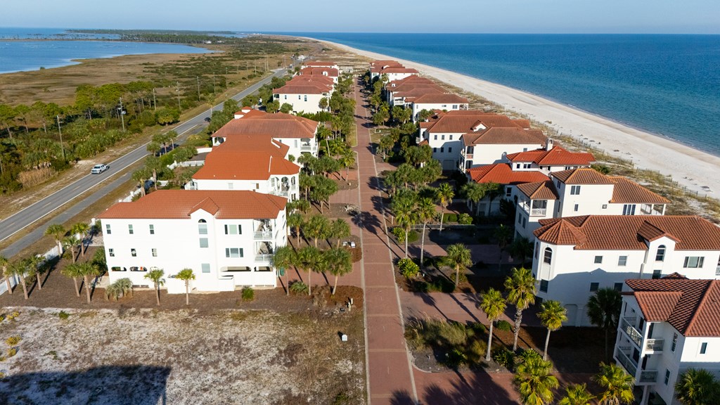 Beachfront homes with red tile roofs line a lane beside the sandy shore.