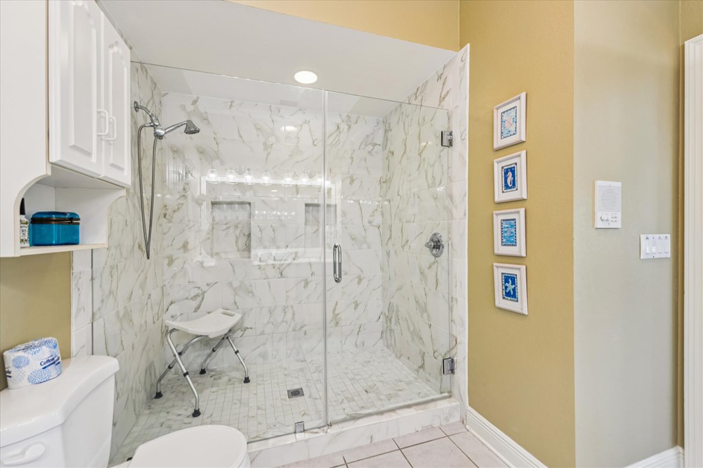 Bathroom with a glass-enclosed marble-look shower, handheld showerhead, and stool.