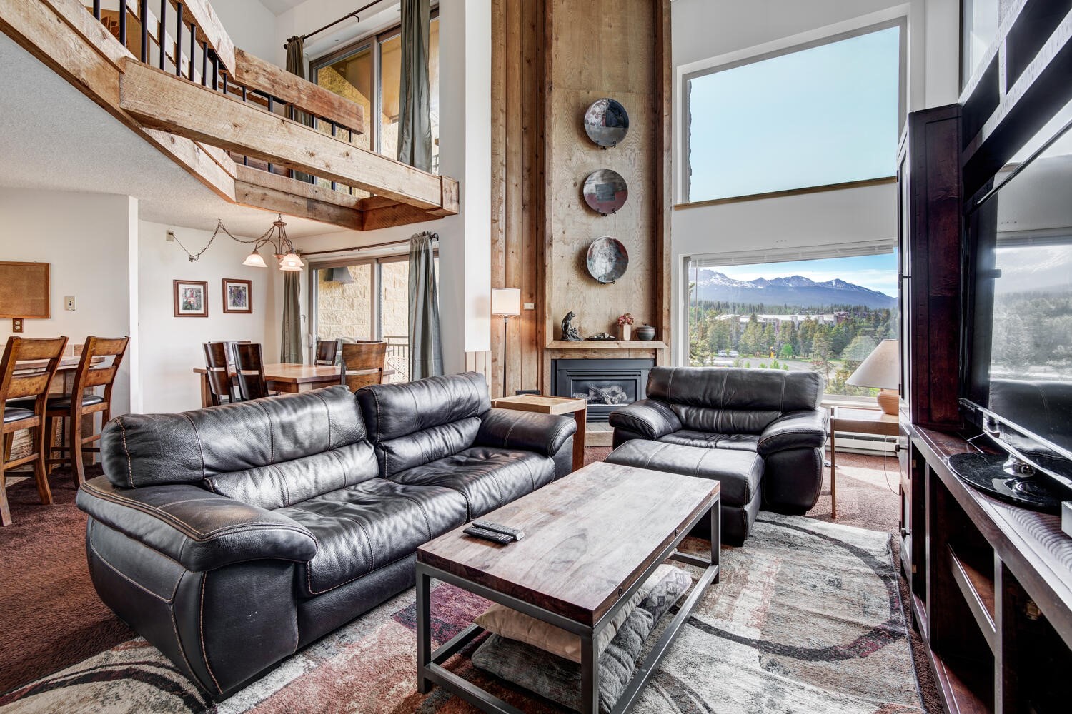 Furnished living room with a fireplace and mountain views through large windows.