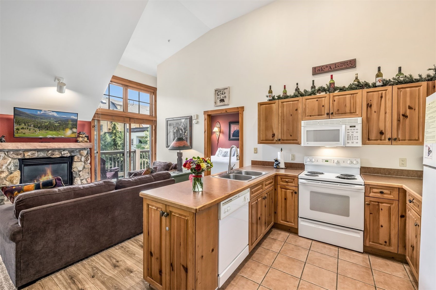 Open-plan kitchen and living room with knotty pine cabinets, an island, and a stone fireplace.