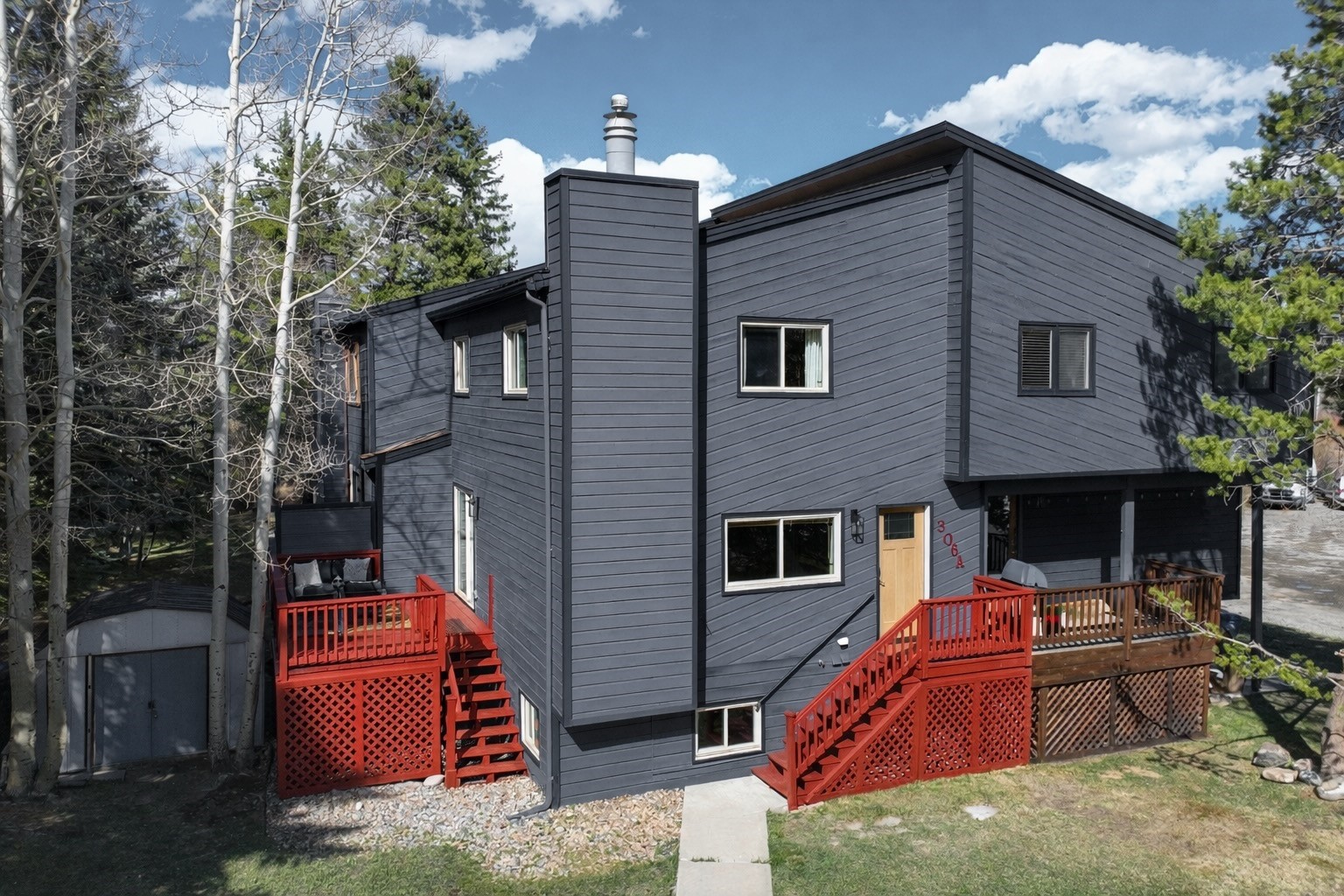 Modern dark-gray home with red decks and stairs, set among trees.