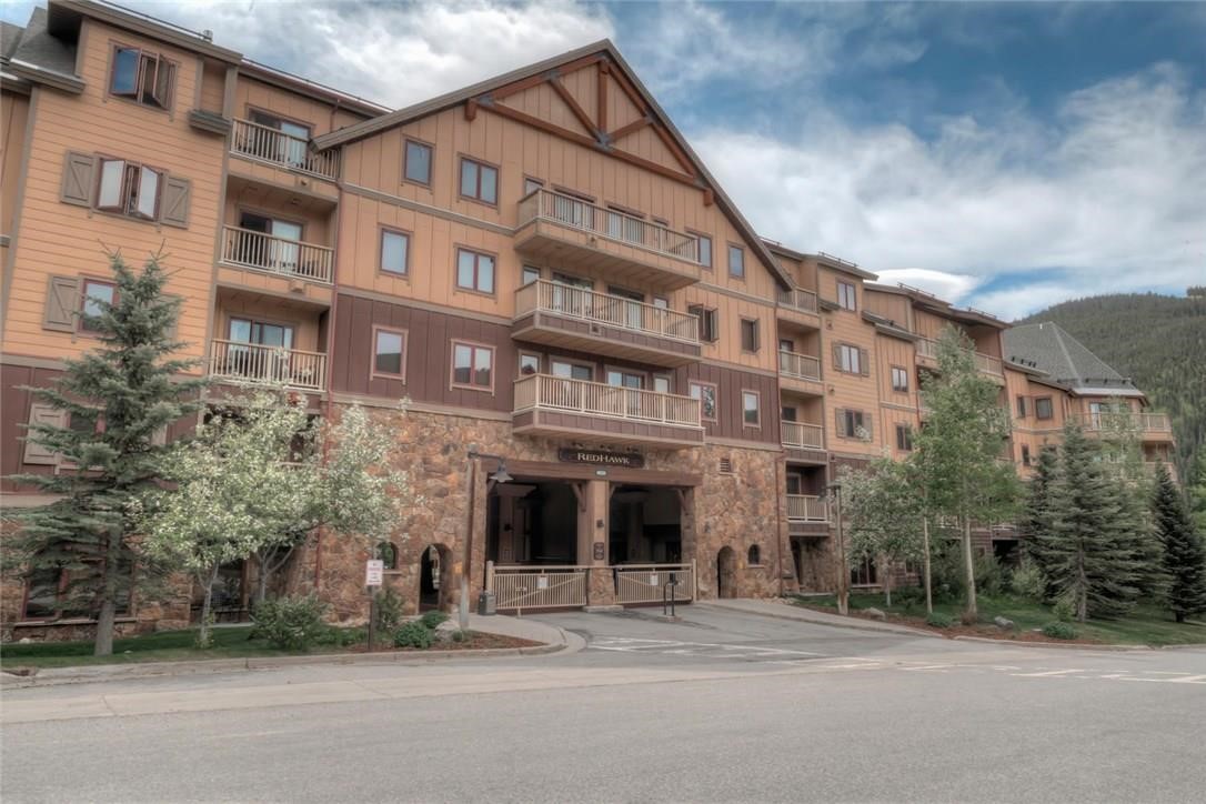 Multi-story condominium building with balconies and a stone entrance, backed by a wooded hillside.