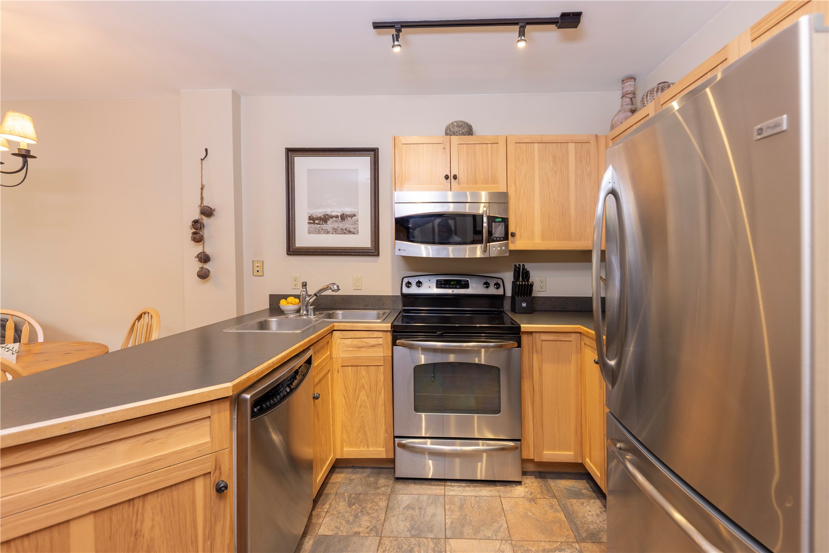 Kitchen with honey-toned wood cabinets, stainless steel appliances, and a dark countertop peninsula.