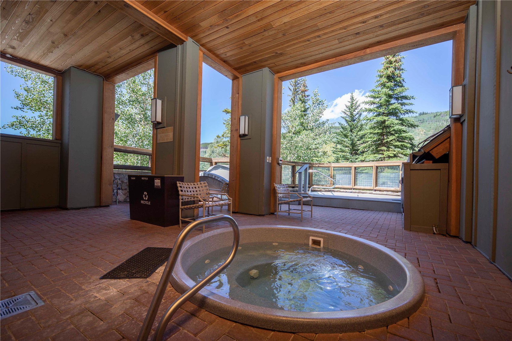 Outdoor hot tub beneath a timber roof, with seating and mountain views.