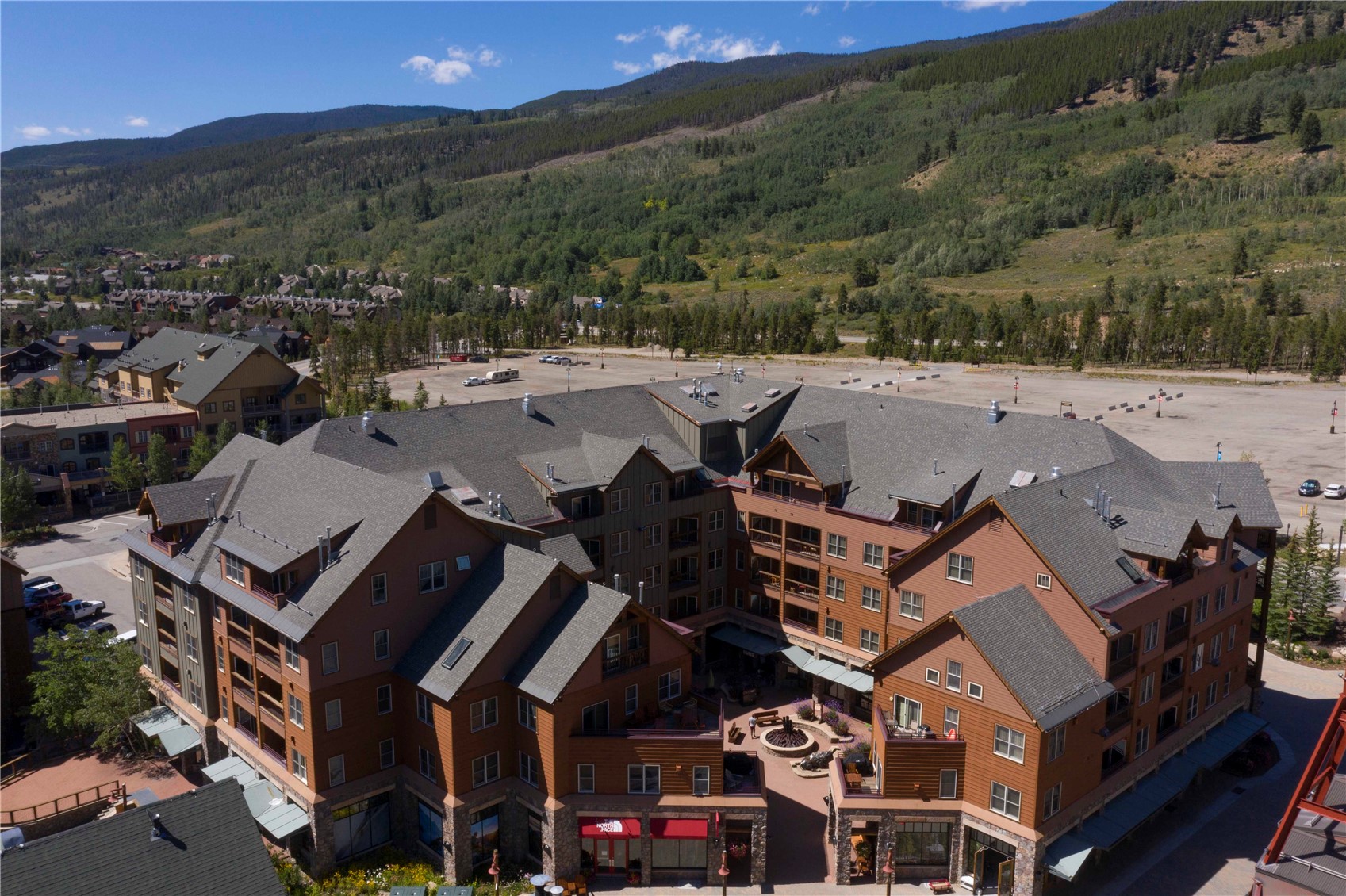 Aerial view of a lodge-style condominium complex with a courtyard, parking area, and forested mountains.