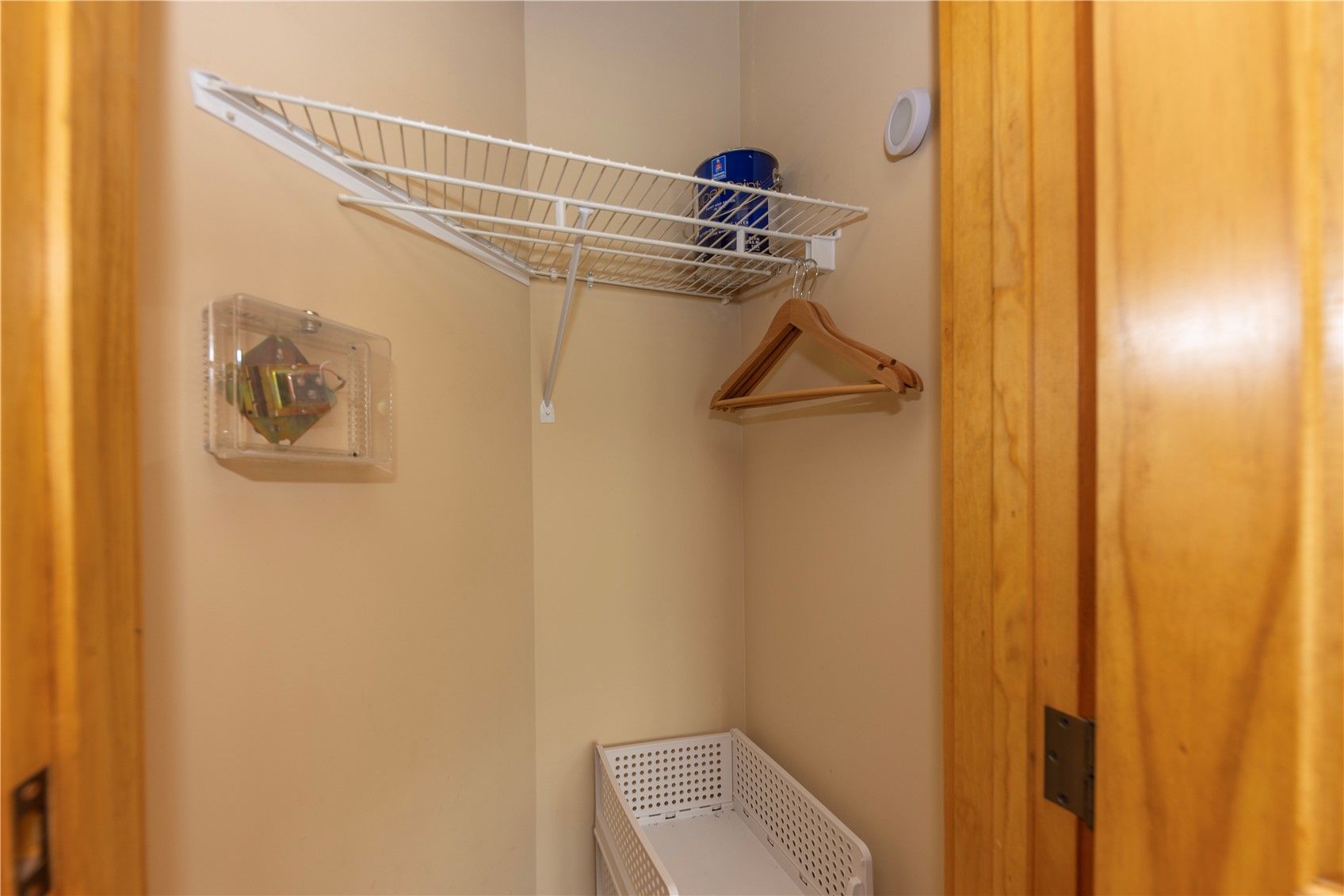 Walk-in closet with a wire shelf, wooden hangers, and a white laundry basket.
