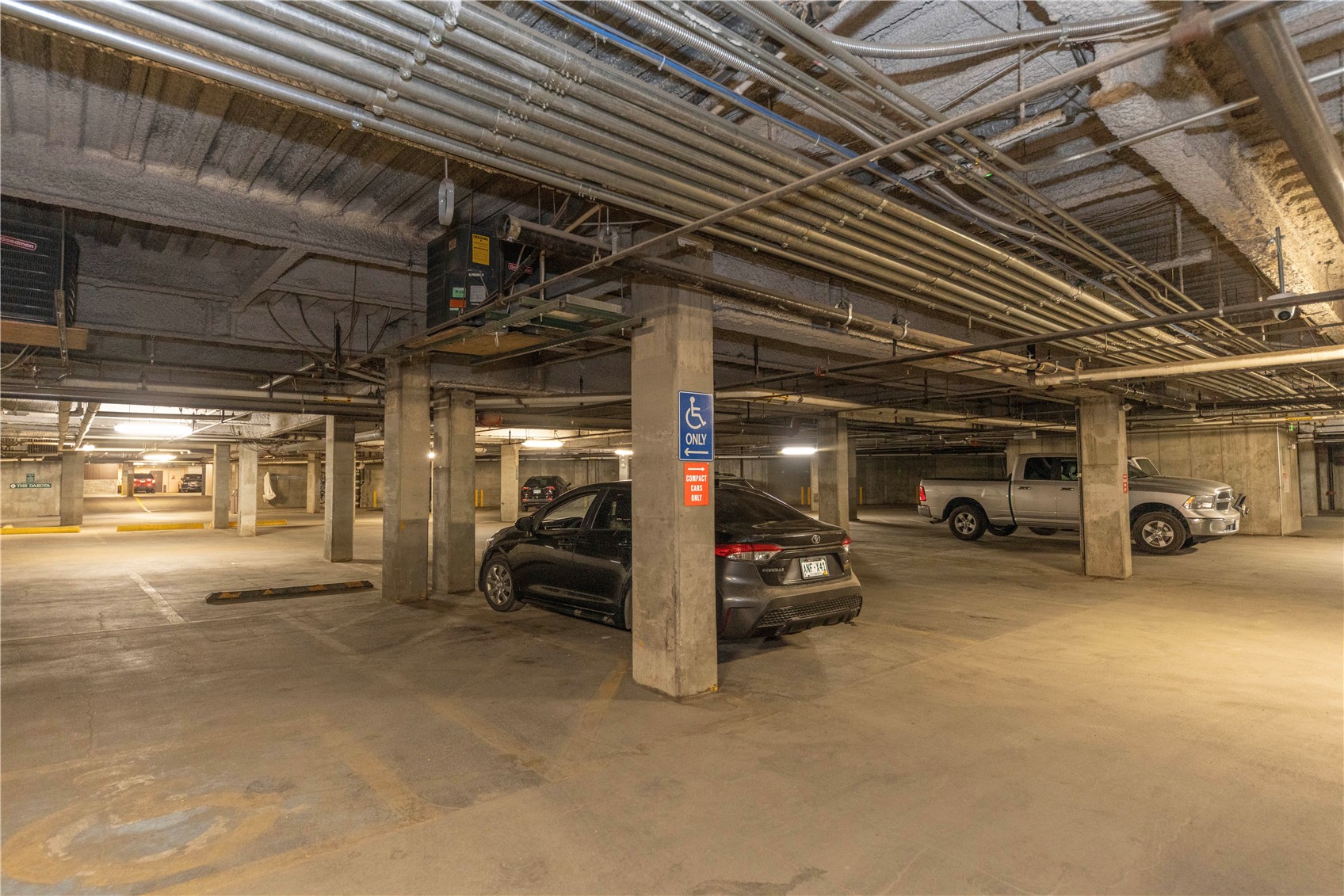 Underground parking garage with parked cars, exposed pipes, and an accessible parking sign.
