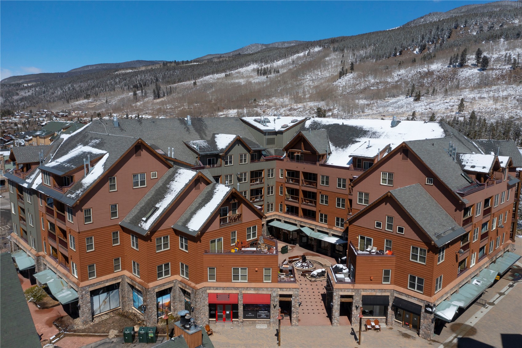 Condominium complex with snow-dusted roofs, backed by a forested mountain.