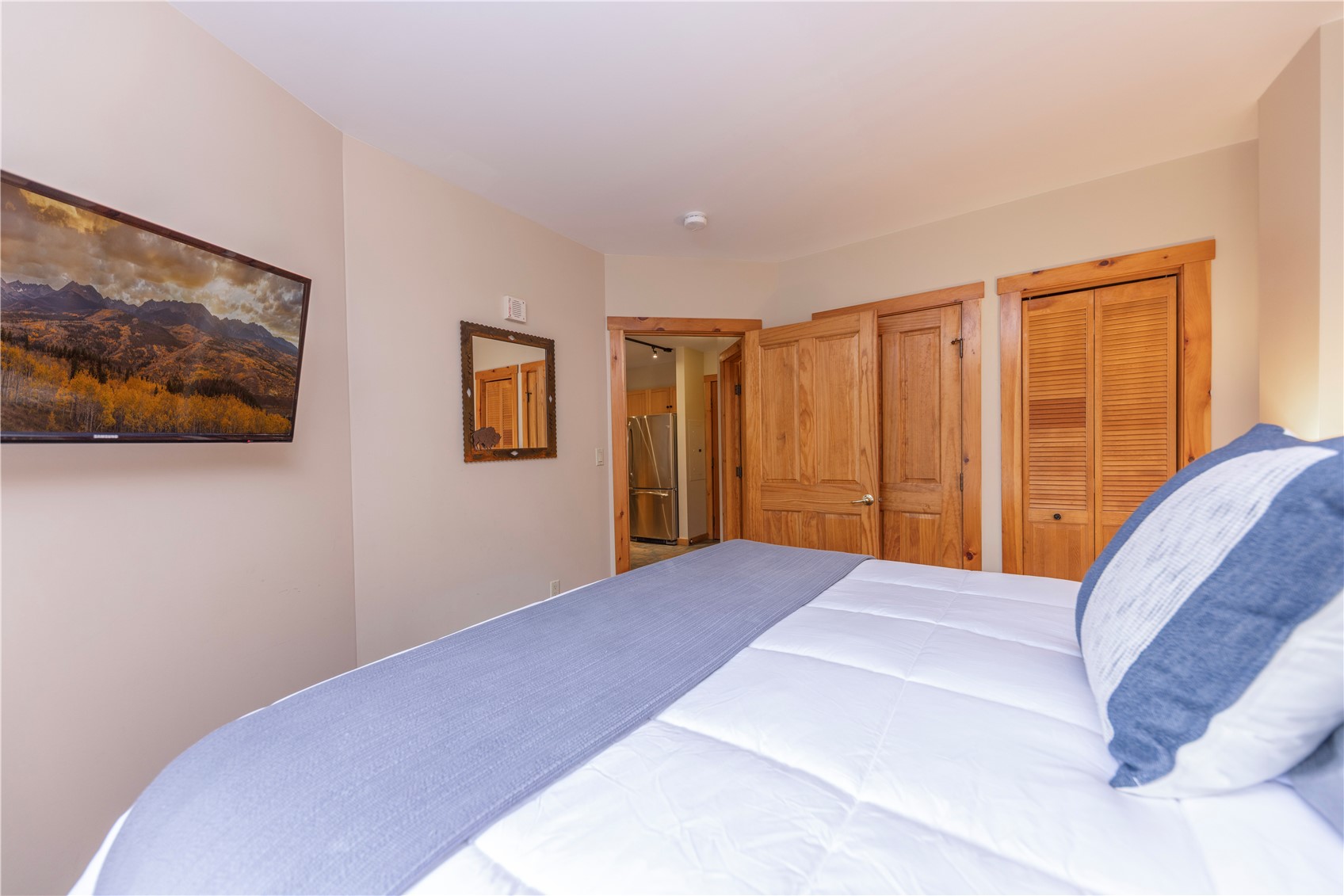 Bedroom with a white bed, blue bedding, warm wood doors, and framed mountain landscape