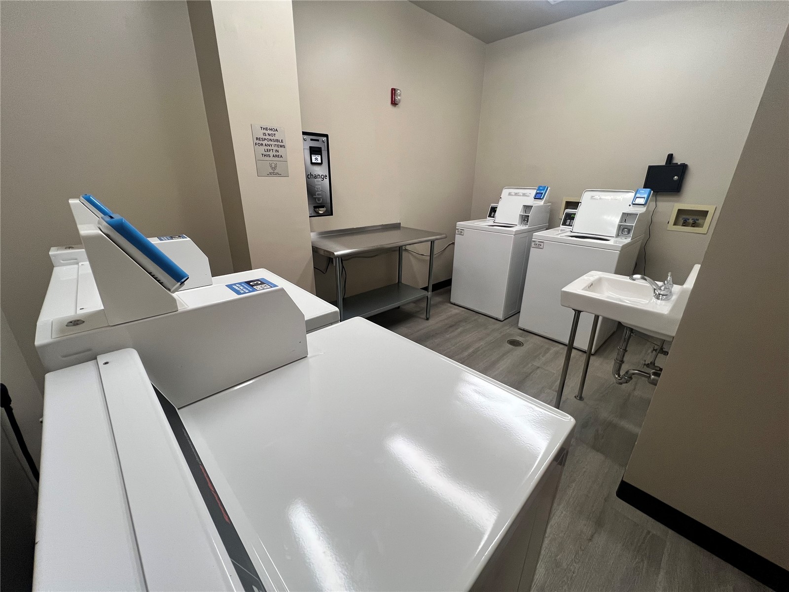 Shared laundry room with multiple washers and dryers, a folding table, and a utility sink.