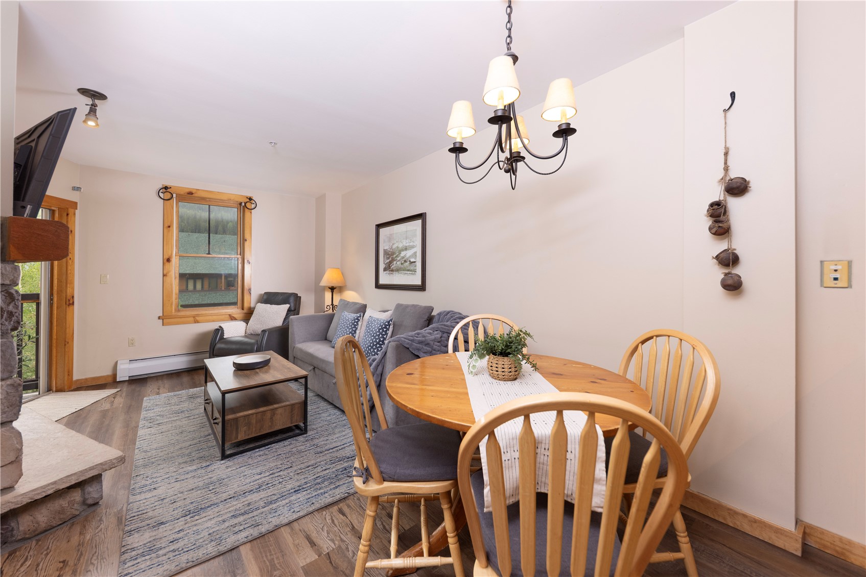 Living and dining area with a gray sofa, round wooden table, and stone fireplace.