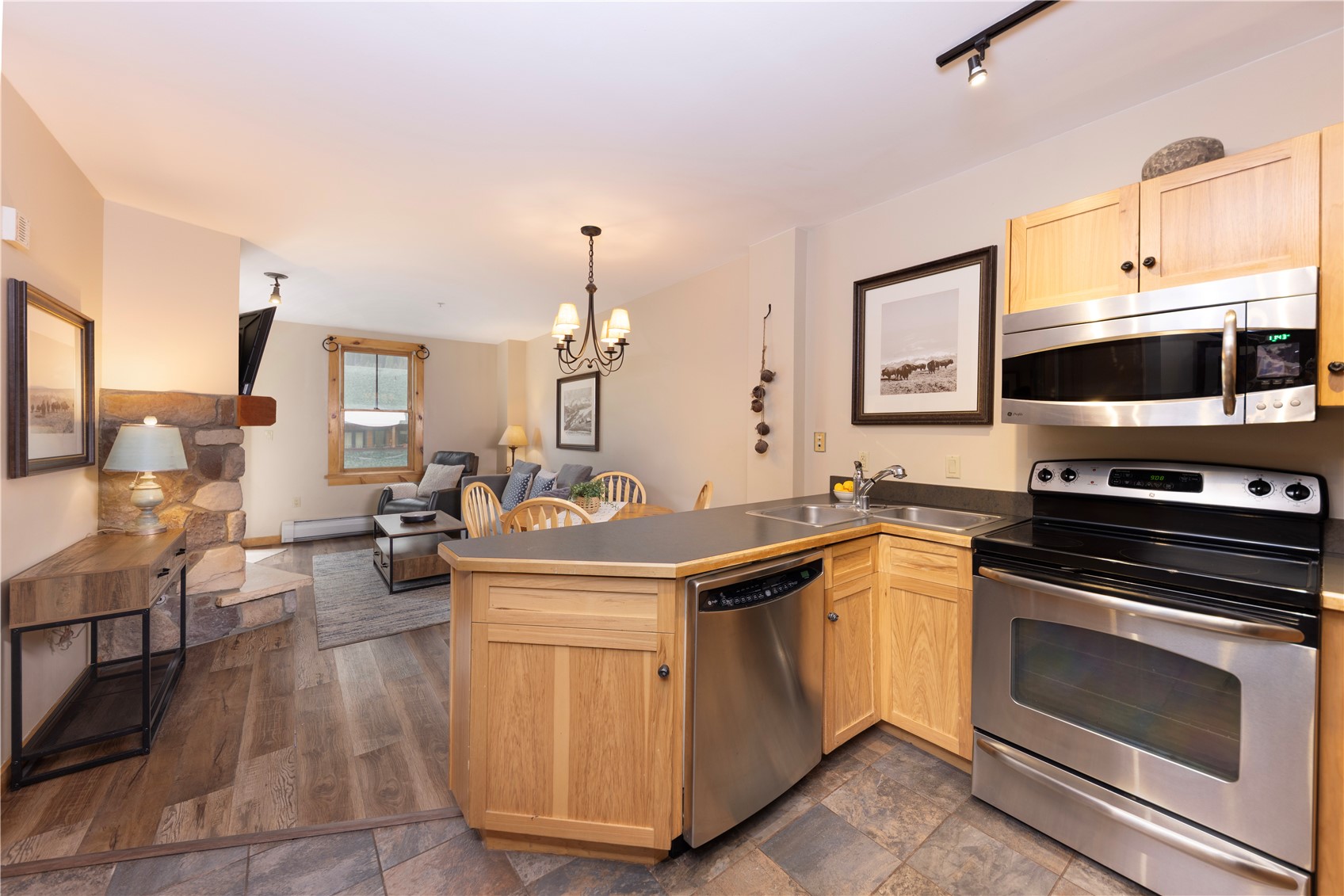 Kitchen with wood cabinets and central island opening to a living area with a stone fireplace.