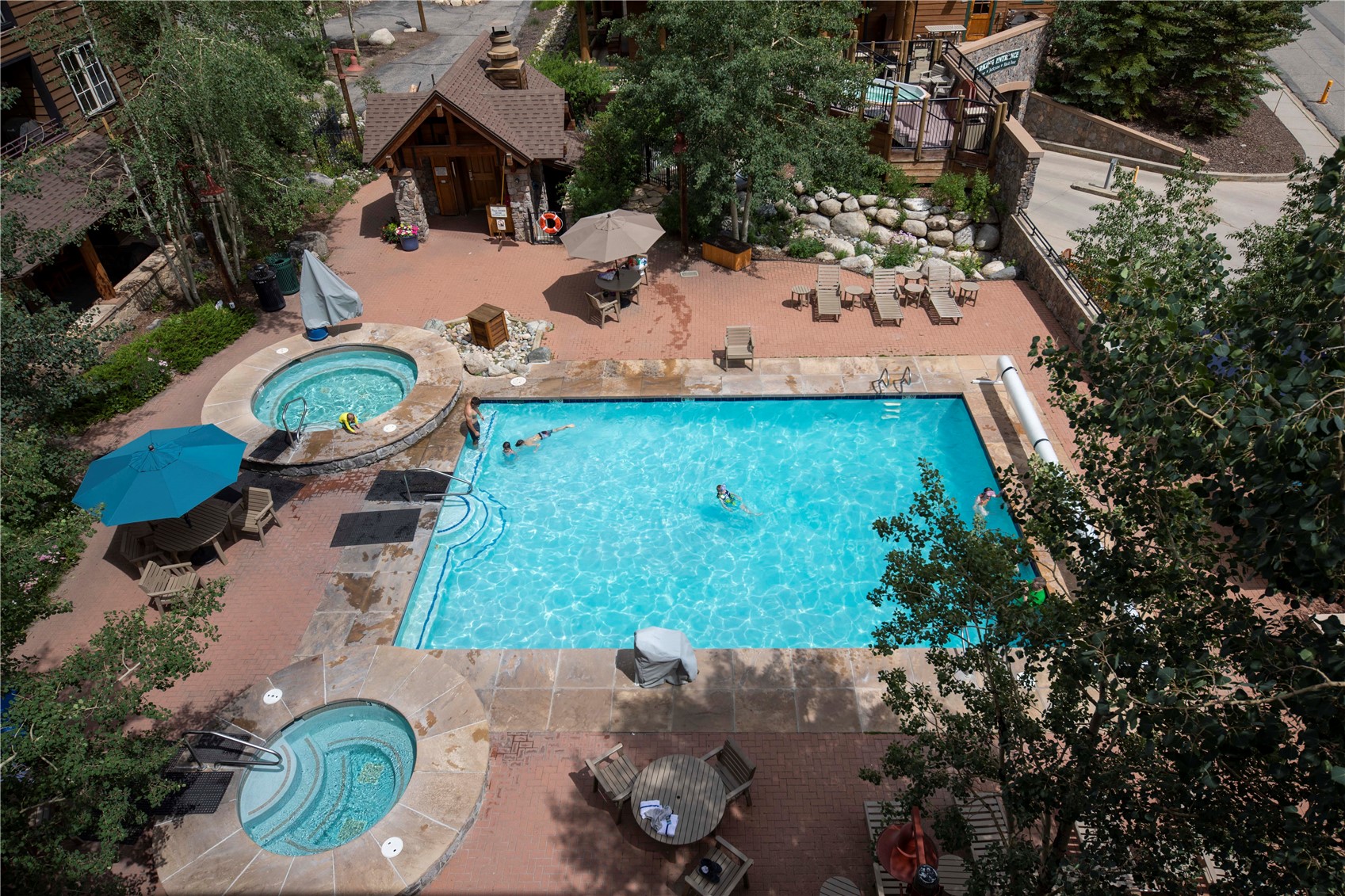 Outdoor pool courtyard with a large swimming pool, two hot tubs, and brick-paved seating areas.