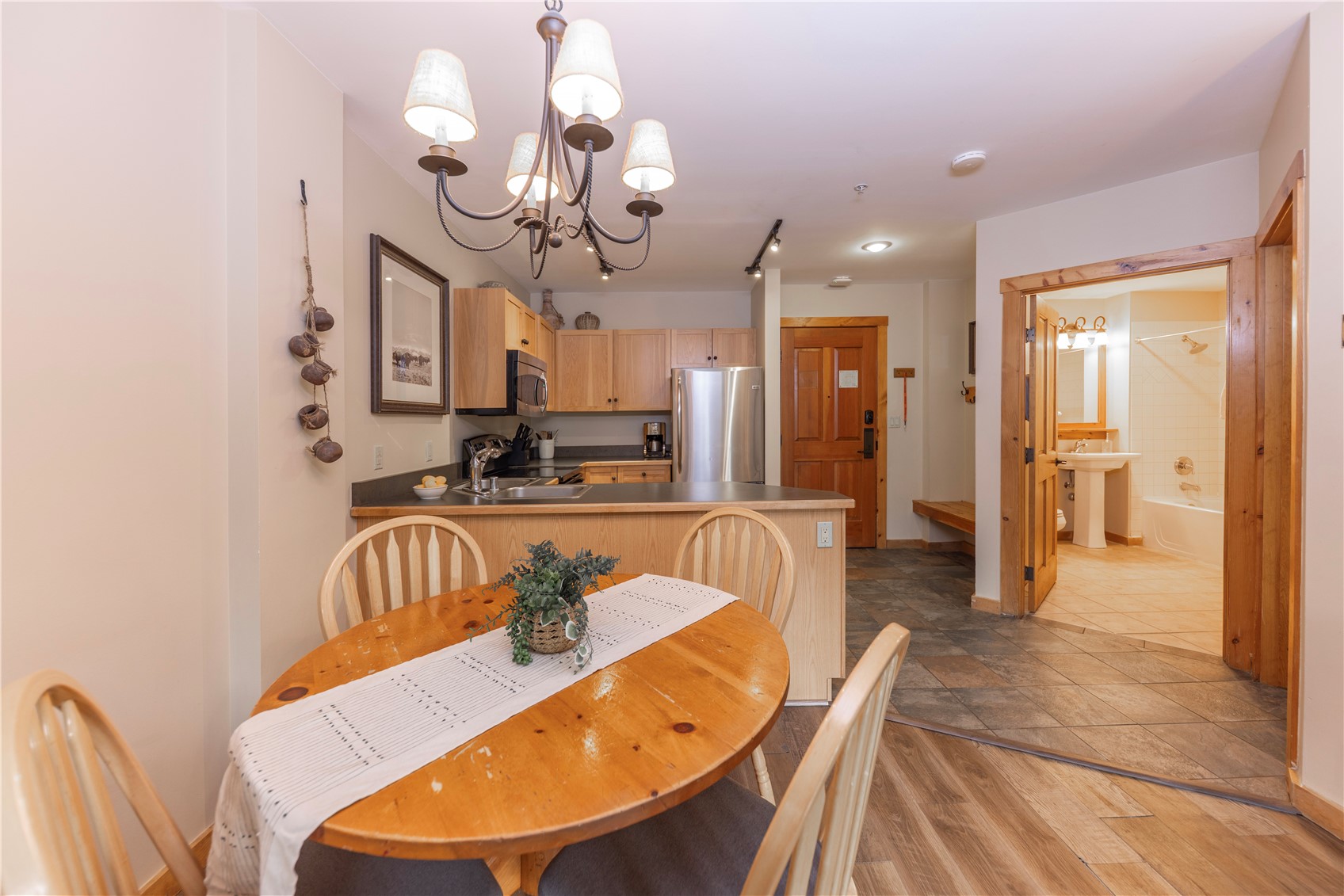 Dining area and kitchen with a round wooden table, light wood cabinets, and an open view into the bathroom.