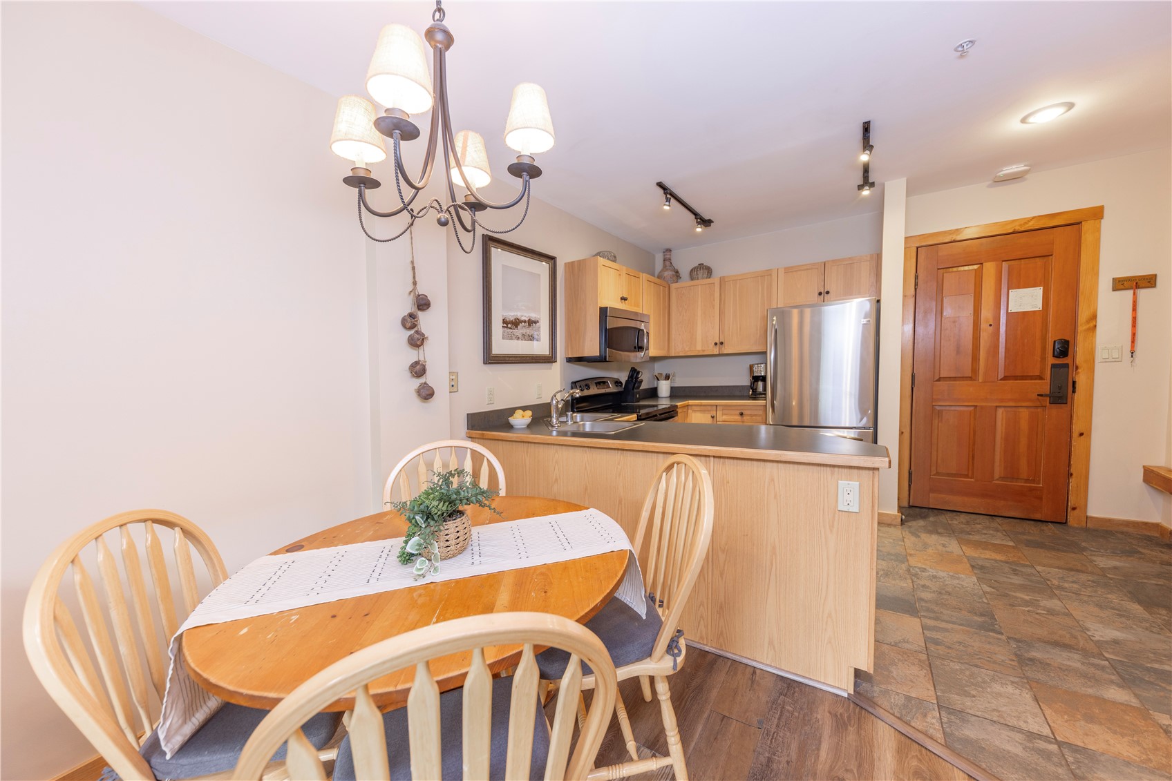 Condo kitchen and dining area with light wood cabinets, stainless steel appliances, and a round wooden table.