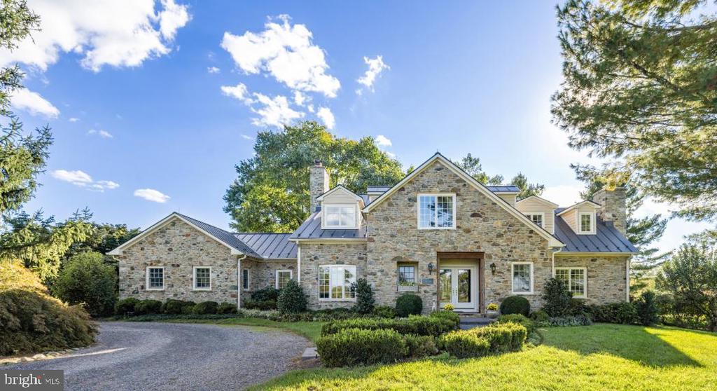 Stone house with a metal roof, landscaped front garden, and curved driveway.