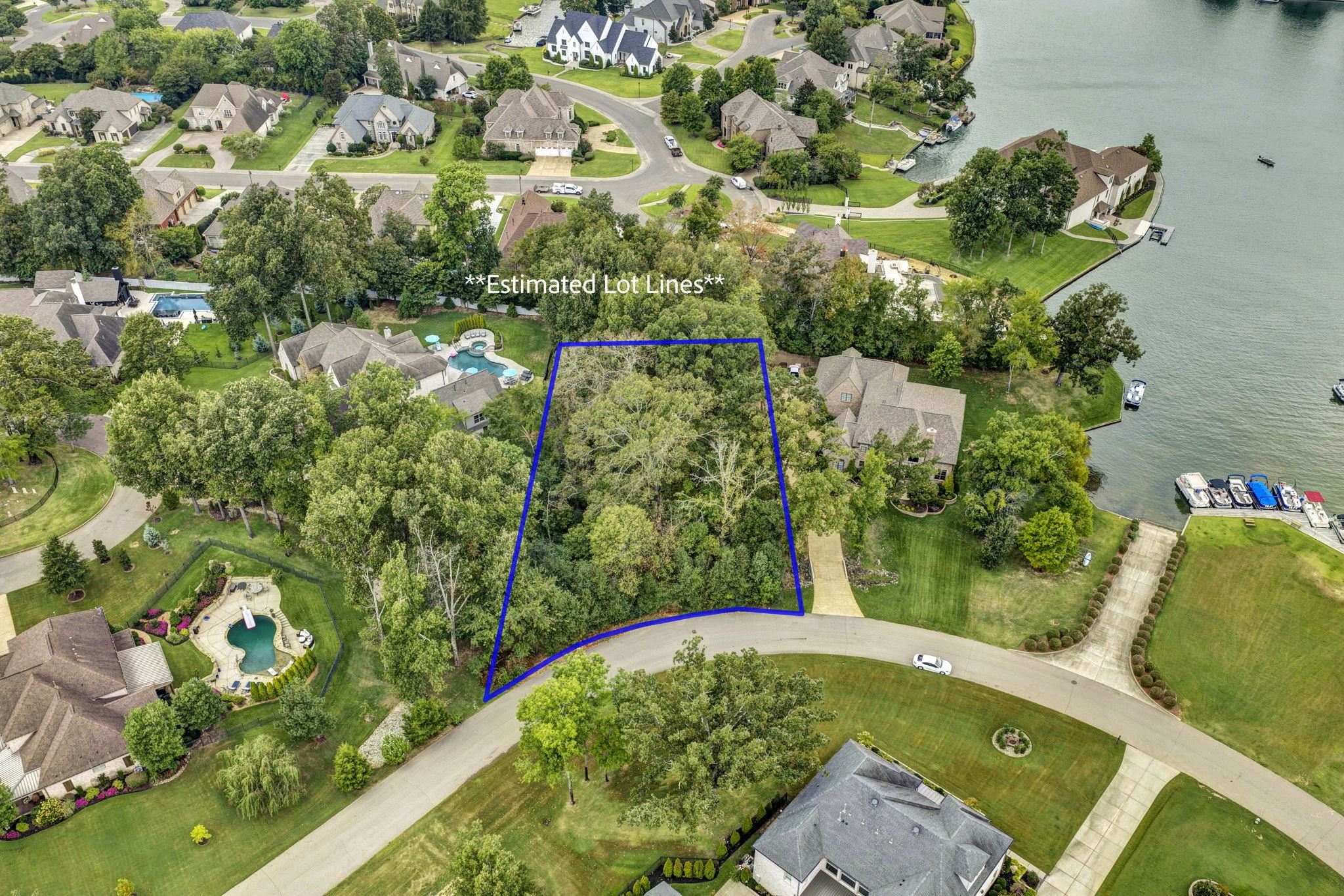 Aerial view of a wooded lot outlined in blue beside a lake and neighborhood homes.