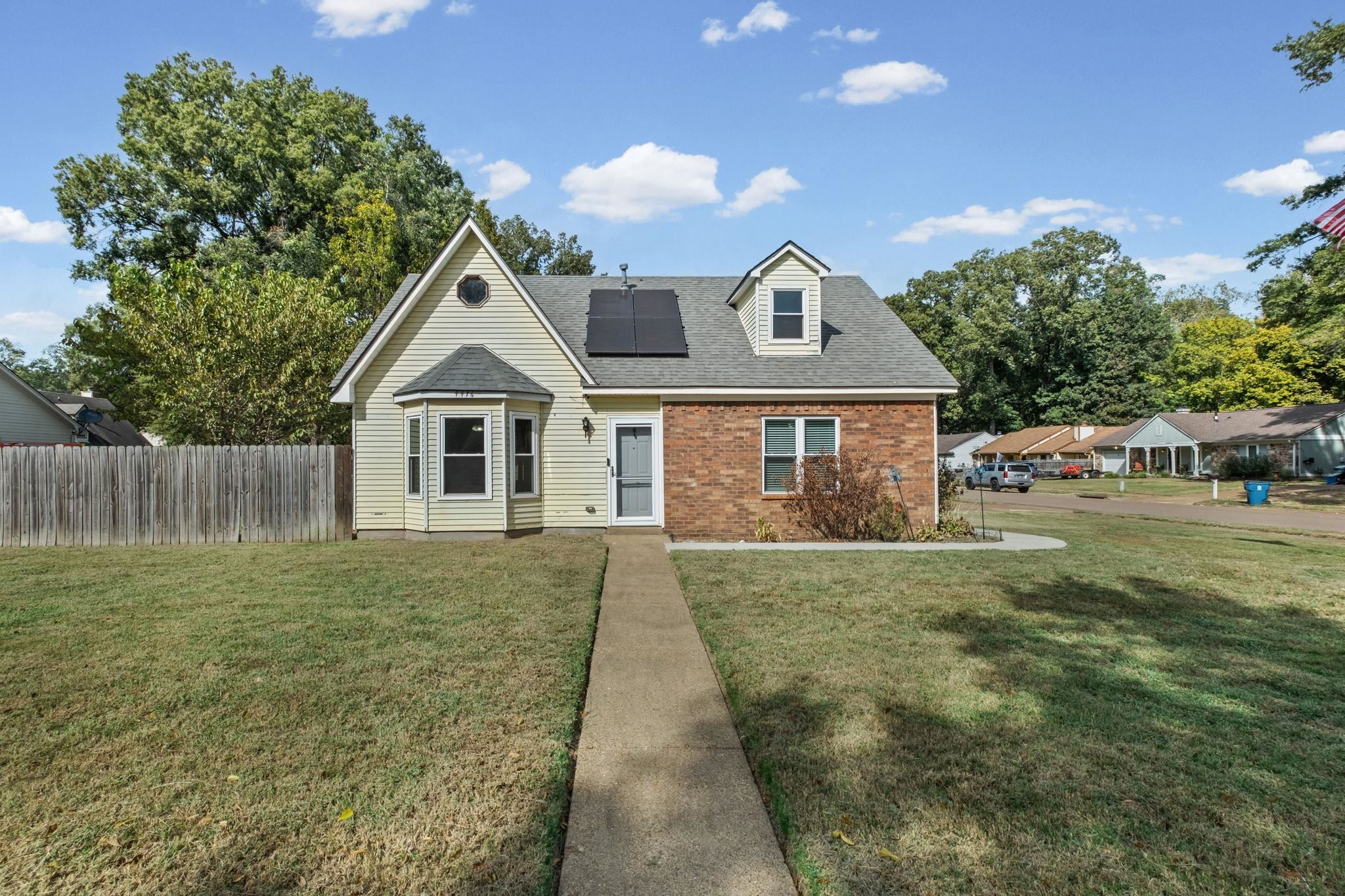 Detached cream-and-brick home with rooftop solar panels and a walkway across the front lawn.