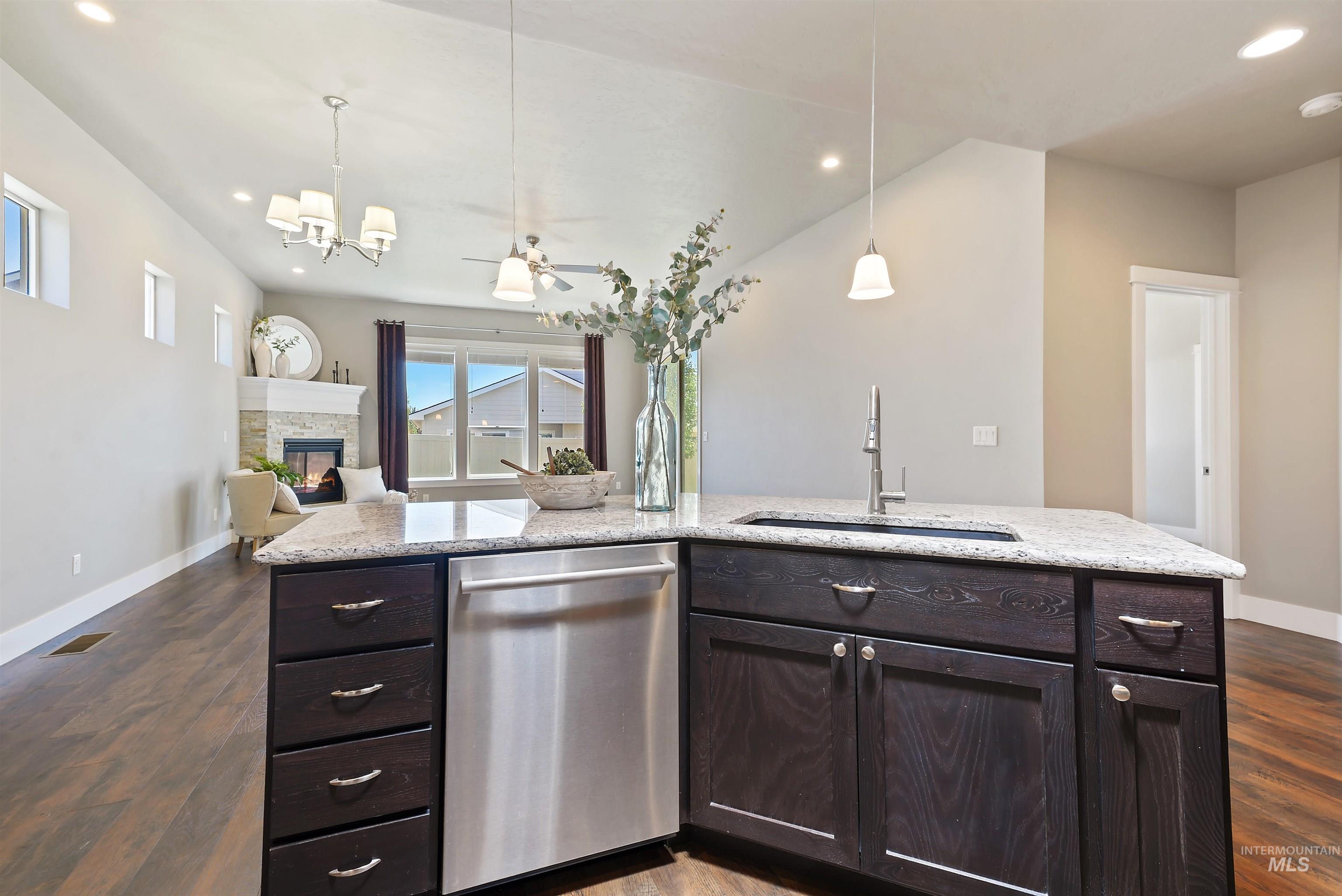 Kitchen island with dark wood cabinets and stone counters overlooking a living area with a stone fireplace.