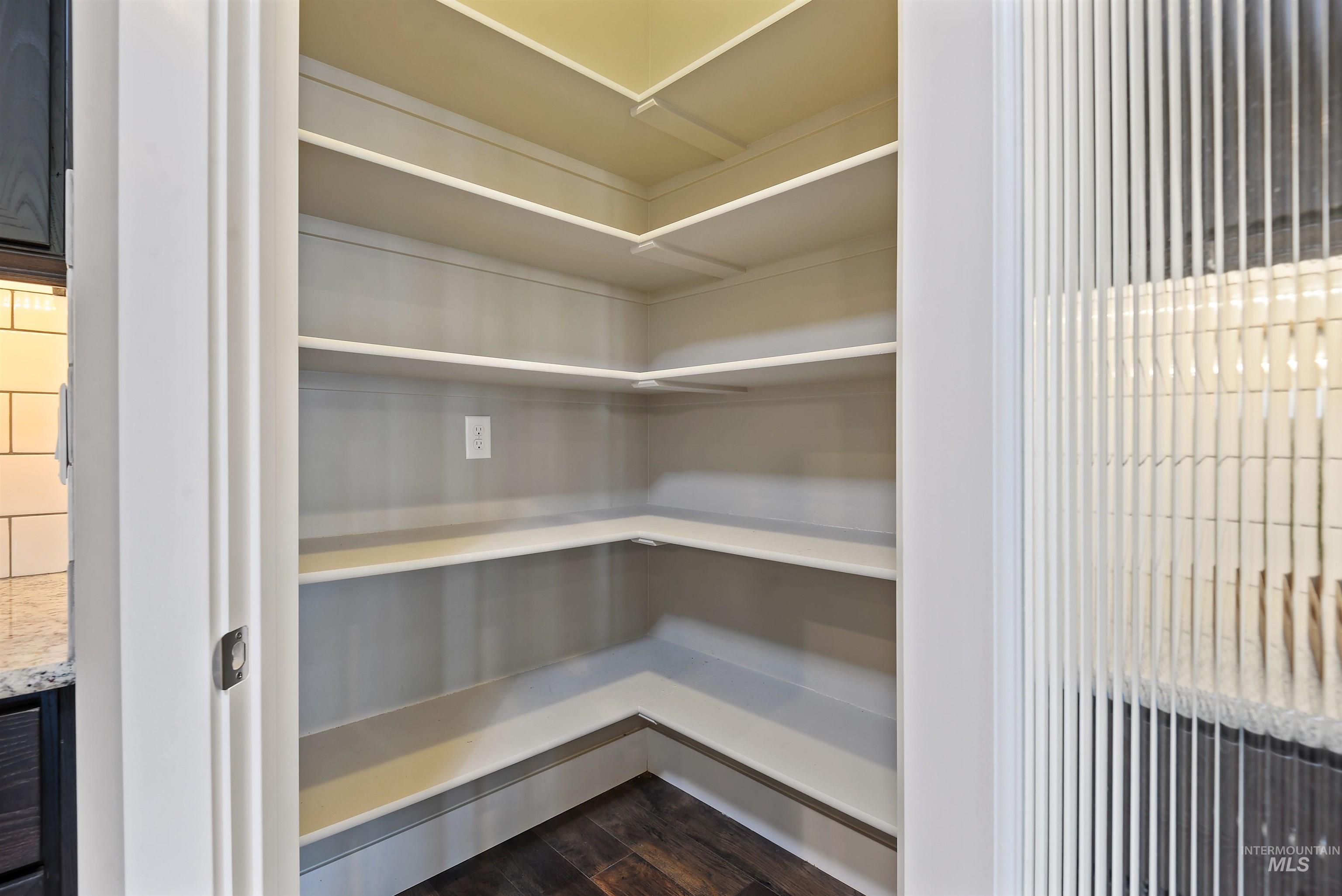 Walk-in pantry with empty white wraparound shelves and dark wood flooring.