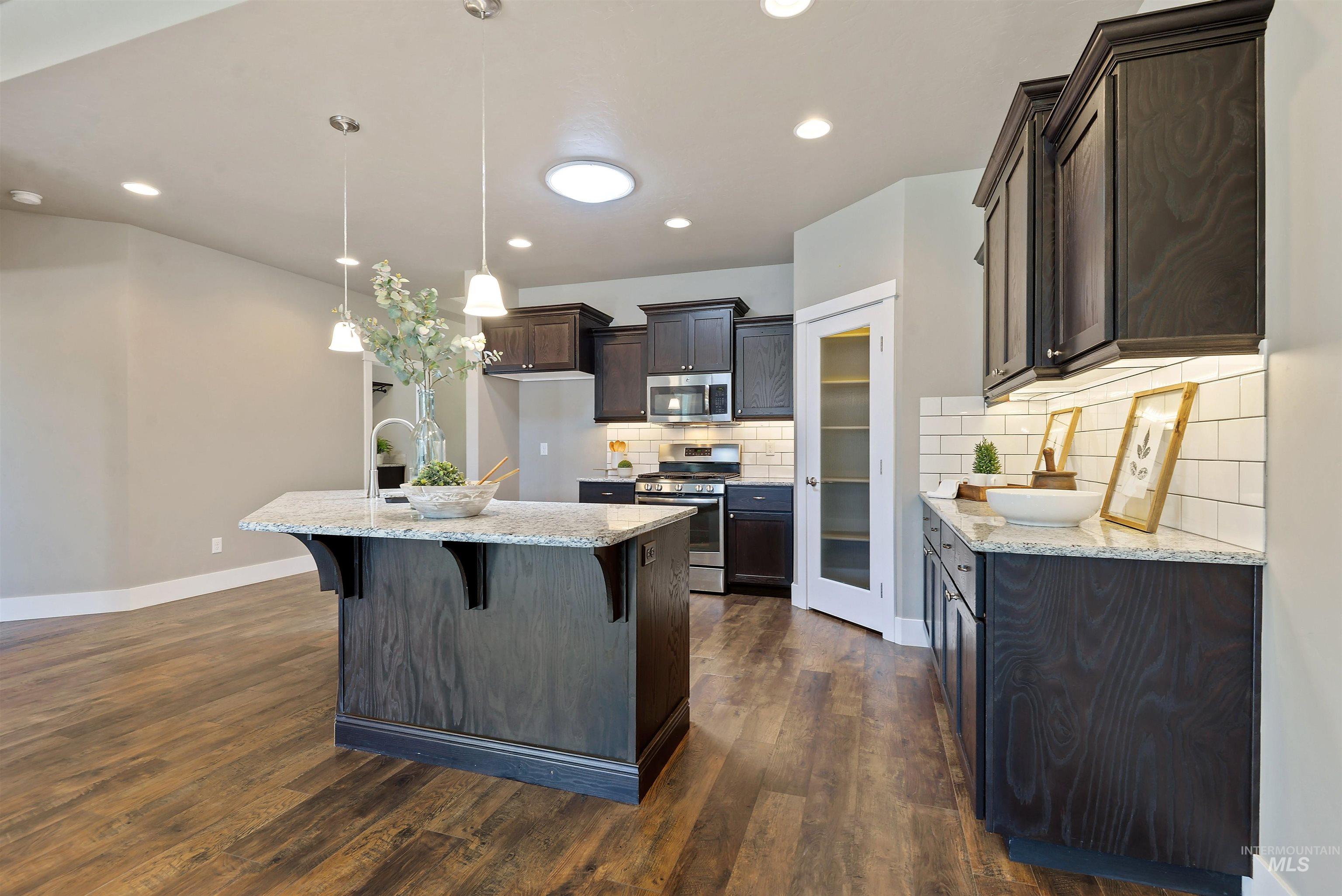 Kitchen with dark cabinets, stainless steel appliances, white tile backsplash, and a granite island.
