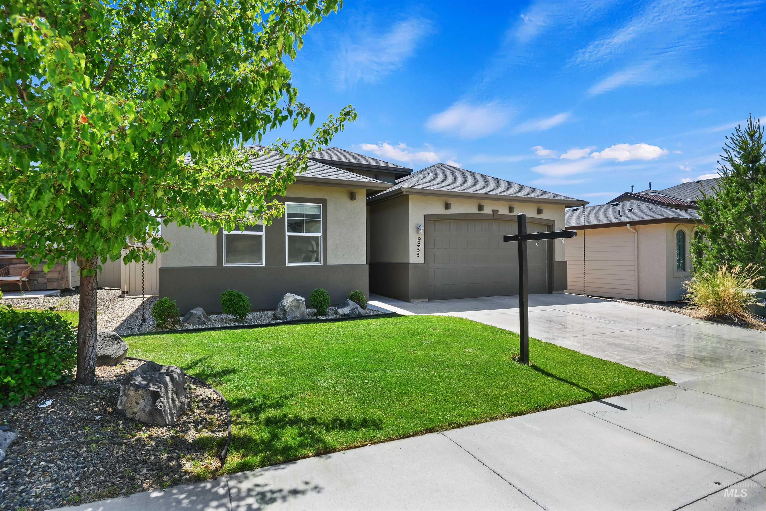 Single-story gray home with a double garage, landscaped lawn, and a mature tree.