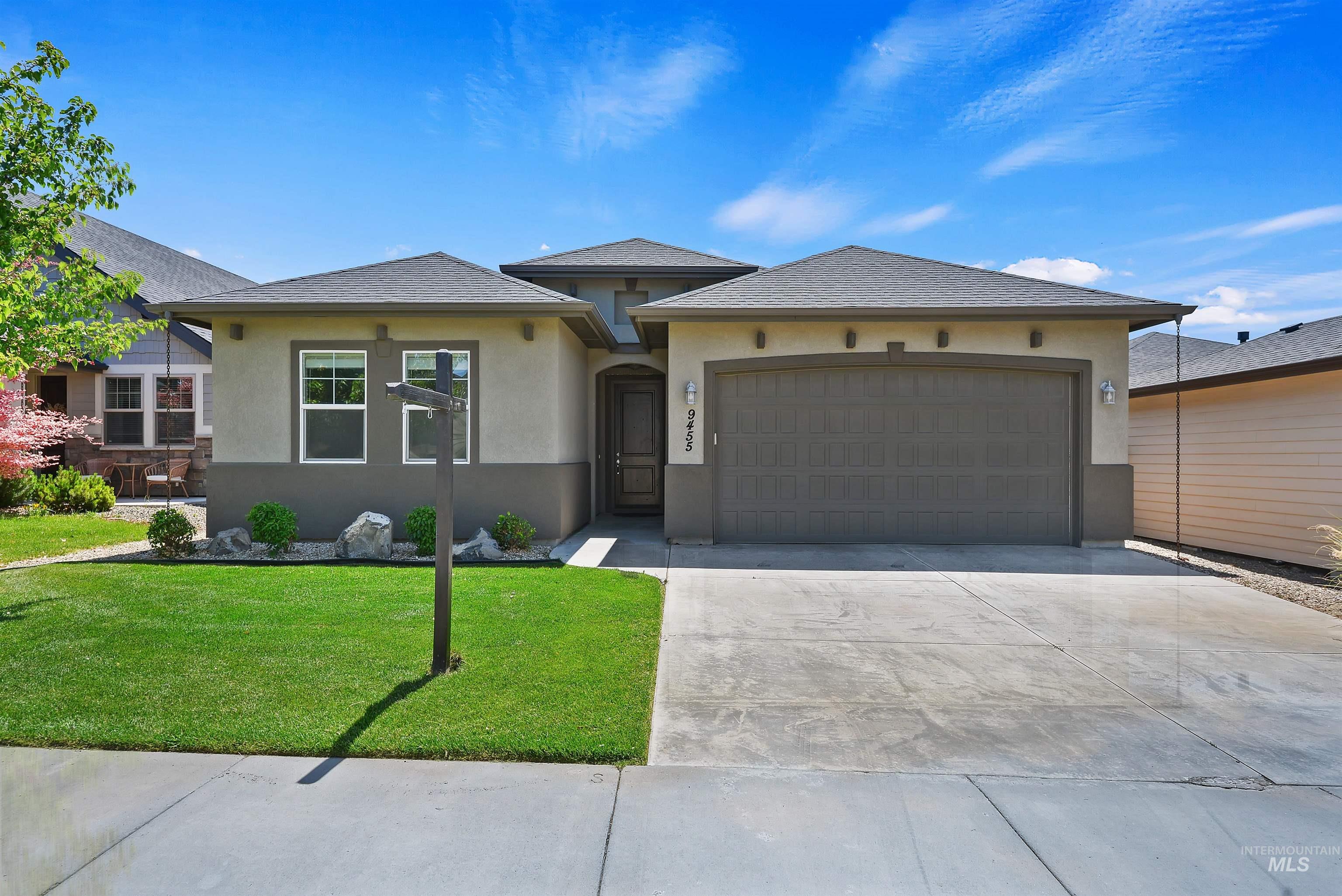 Single-story gray stucco home with a wide double garage, landscaped lawn, and concrete driveway.
