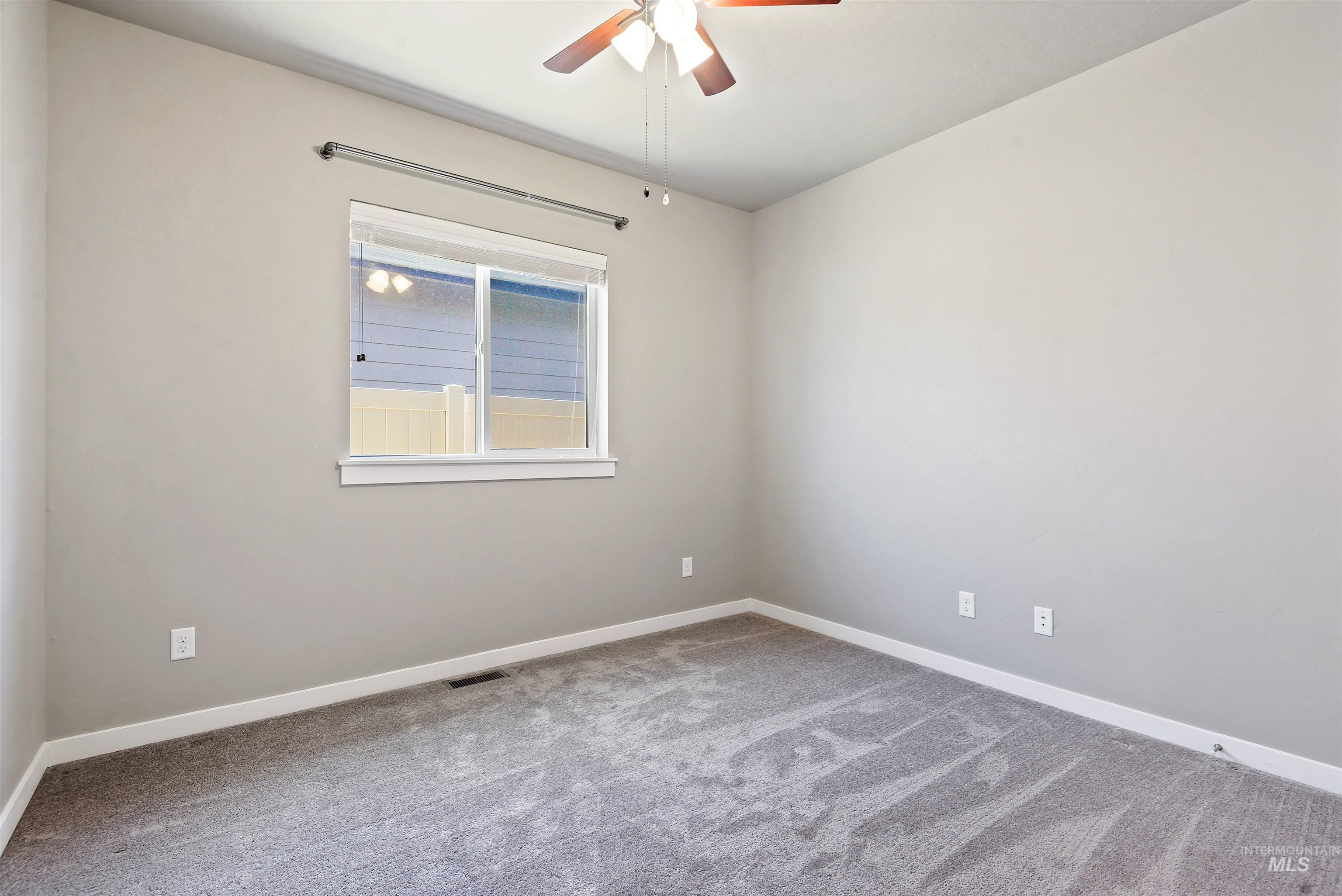 Empty bedroom with gray carpet, a window with blinds, and a ceiling fan with lights.