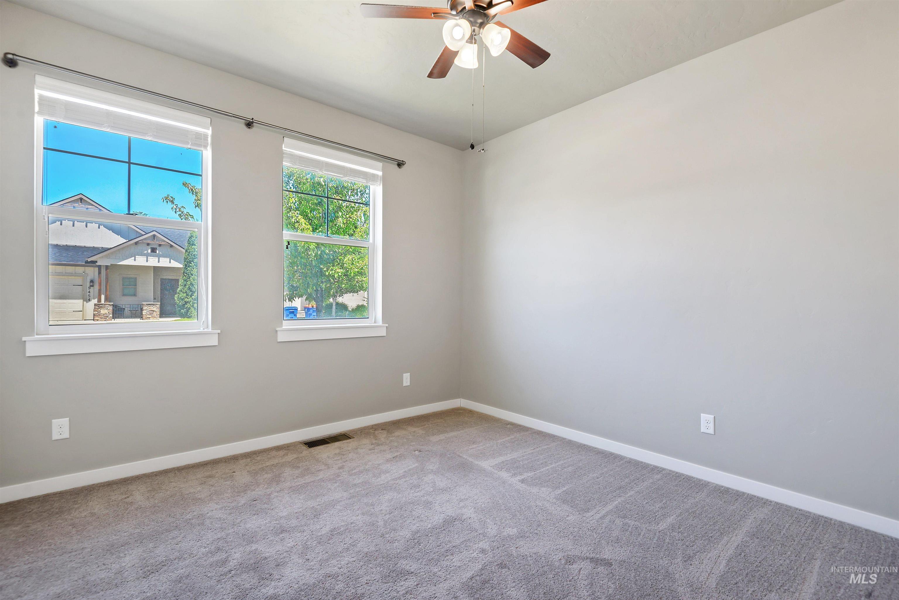 Empty bedroom with gray carpet, two windows, and a ceiling fan.
