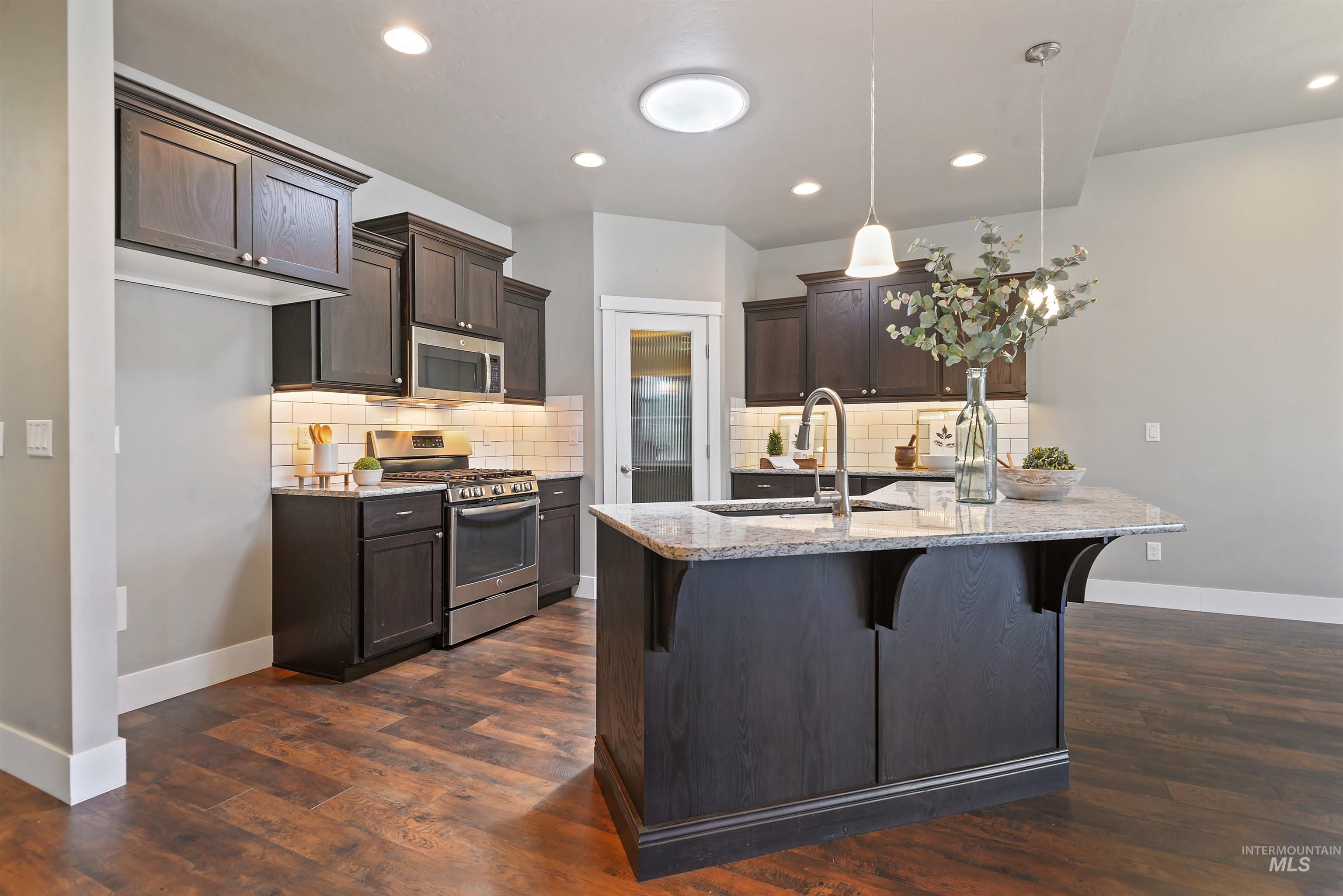 Kitchen with dark wood cabinets, subway tile backsplash, and a large granite island with sink.