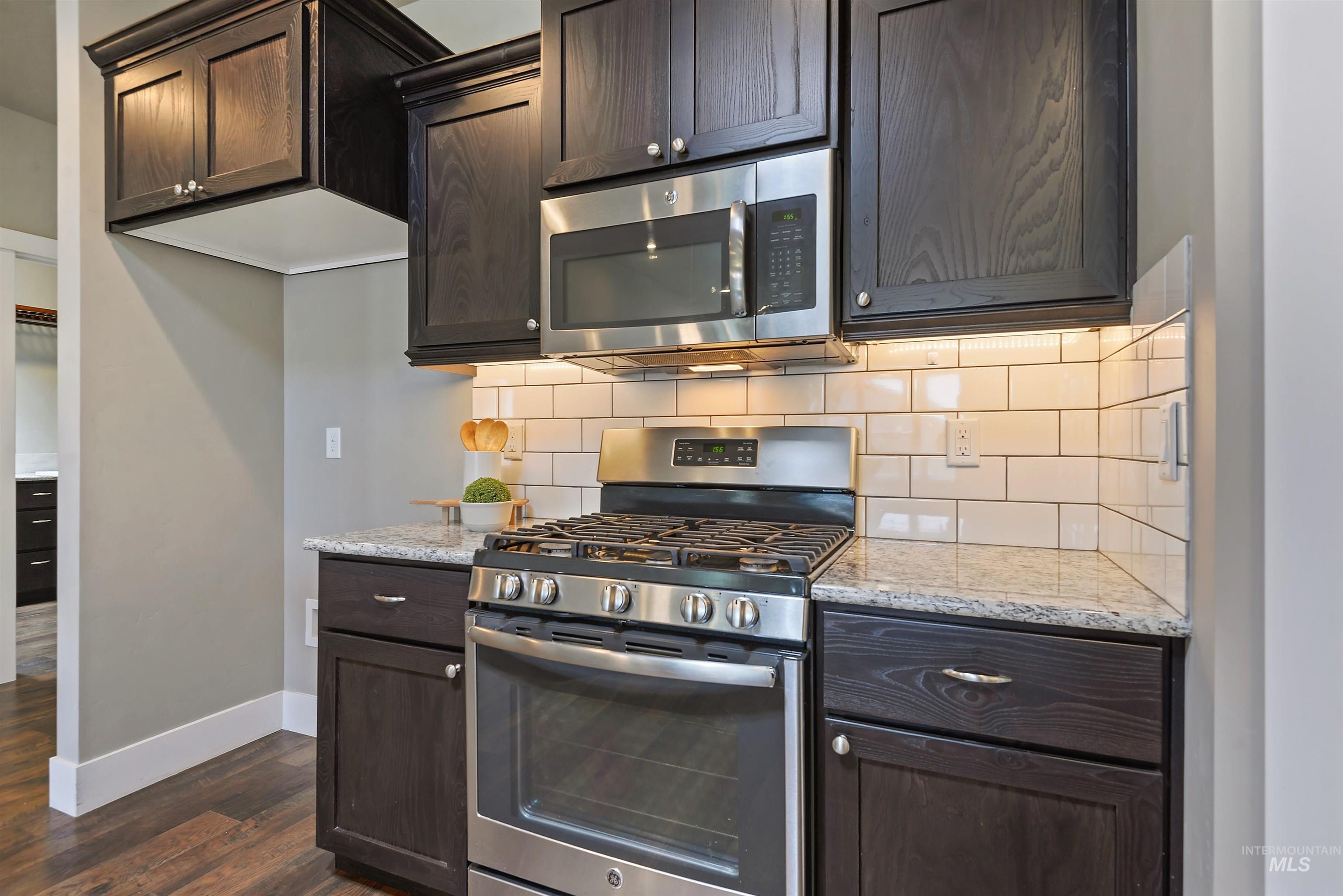 Kitchen with dark wood cabinets, stainless steel gas range, granite counters, and white subway tile backsplash.