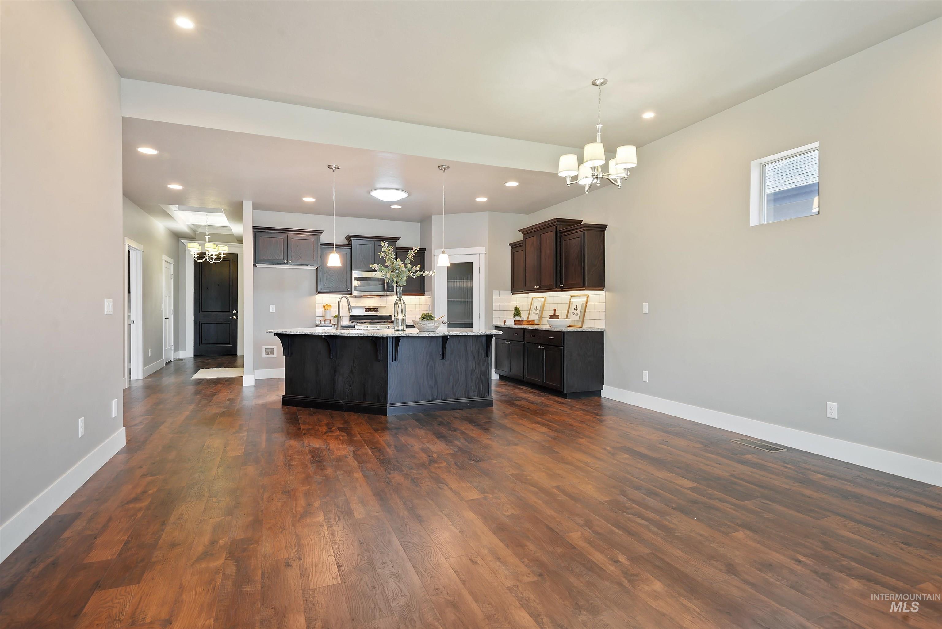 Open kitchen with dark cabinets, a large island, and warm wood flooring in an unfurnished space.