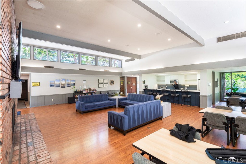 Spacious common room with blue sofas, wood floors, and a kitchenette and dining area.