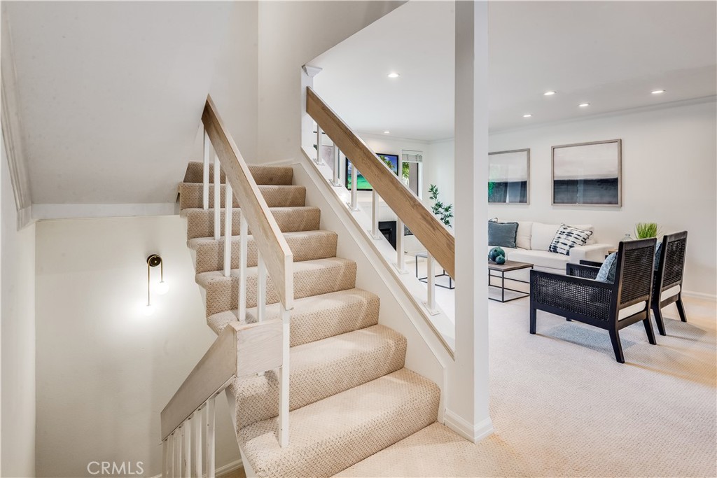 Carpeted staircase with light wood railings beside a bright, furnished living room.