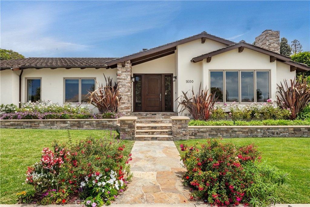 Single-story home with stone accents, a central entry path, and colorful landscaped flower beds.