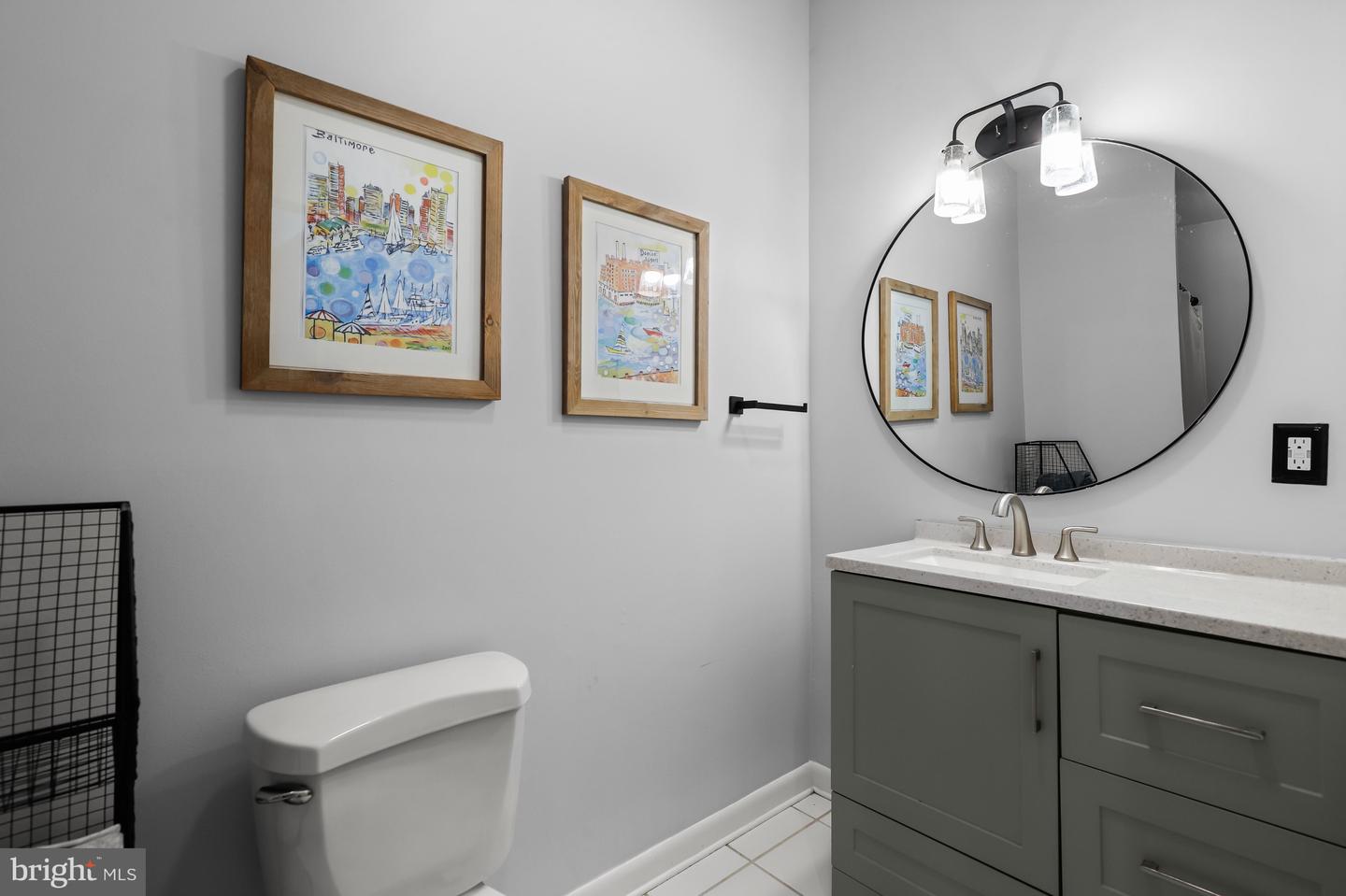Bathroom with a gray vanity, round mirror, and framed Baltimore artwork.