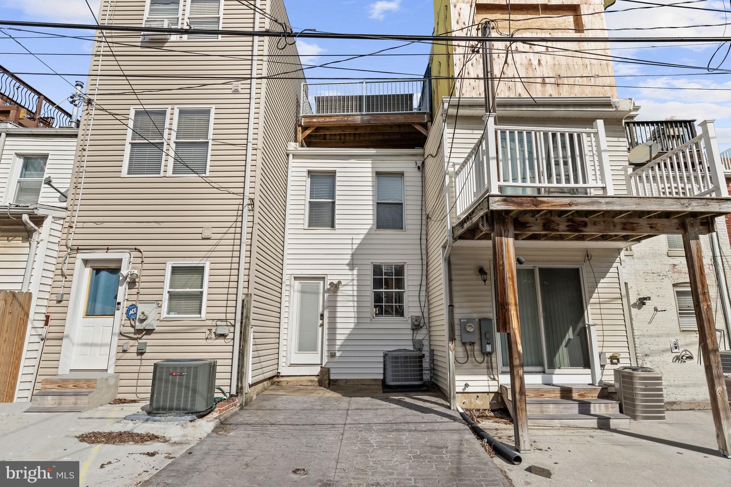 Rear of a light-sided rowhouse with elevated wooden decks and a paved courtyard.